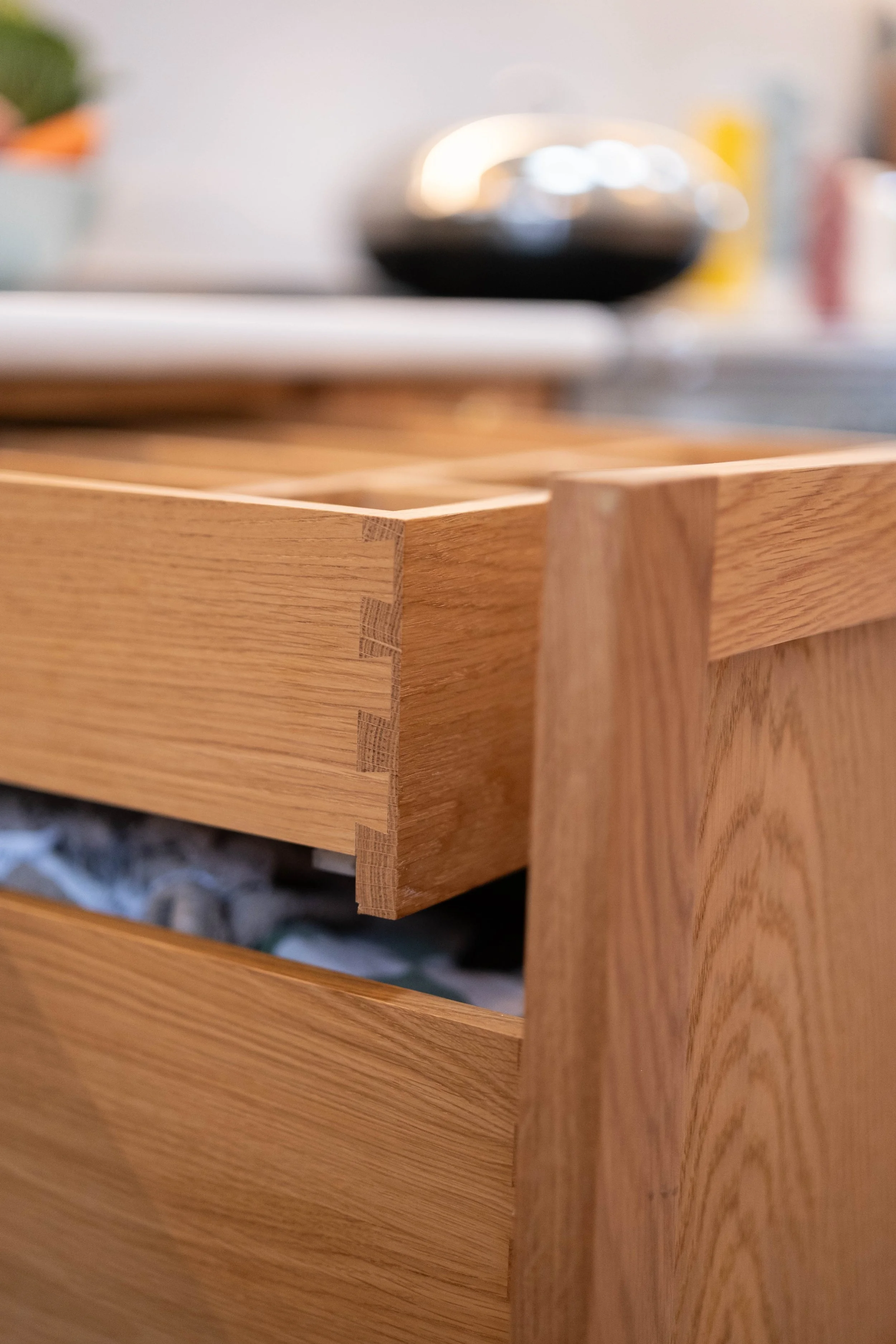 Close-up of a wooden drawer with dovetail joinery, partially open with a glimpse of a blurred object inside.