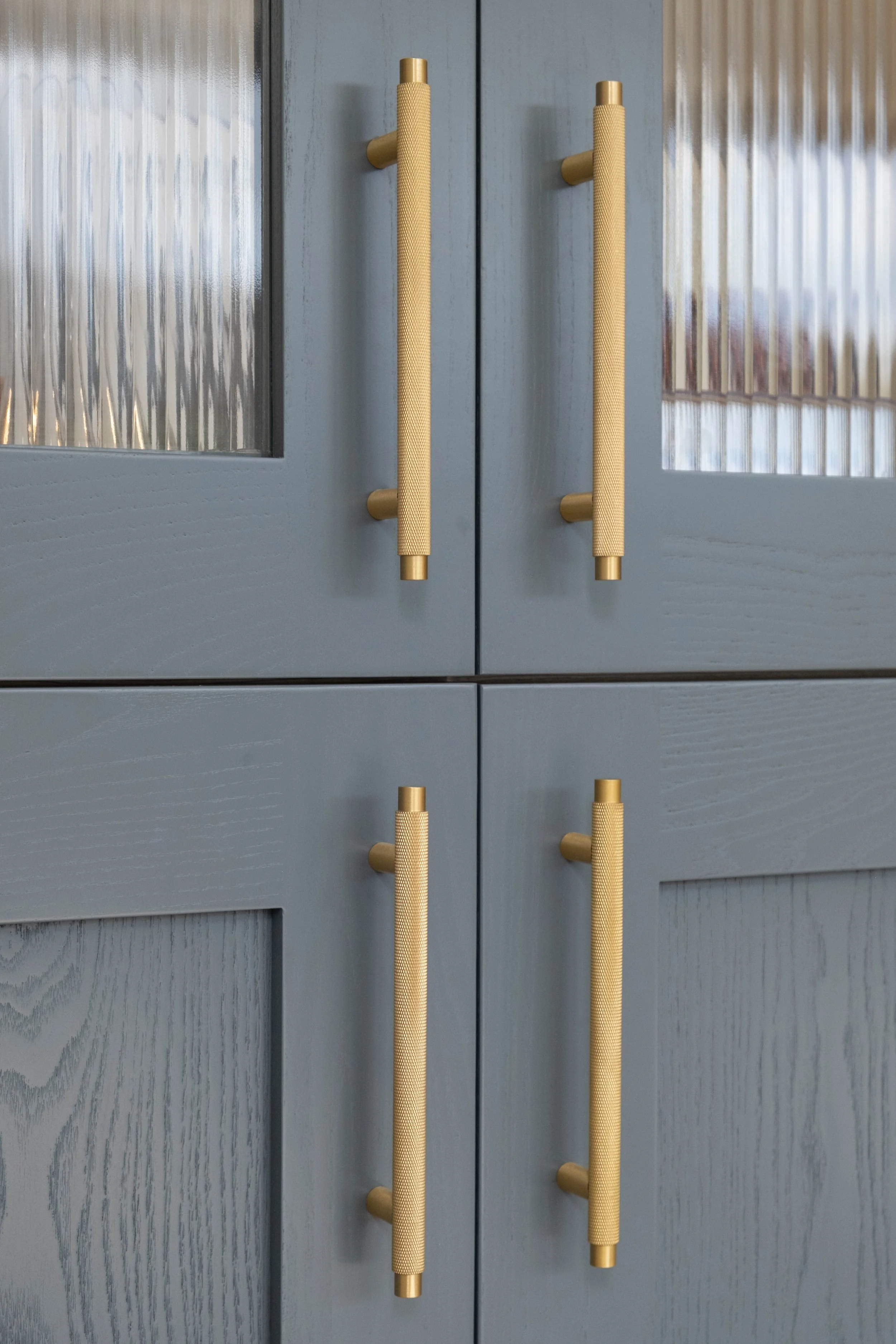 Close-up of two light gray doors with vertical textured glass panels and gold handles.