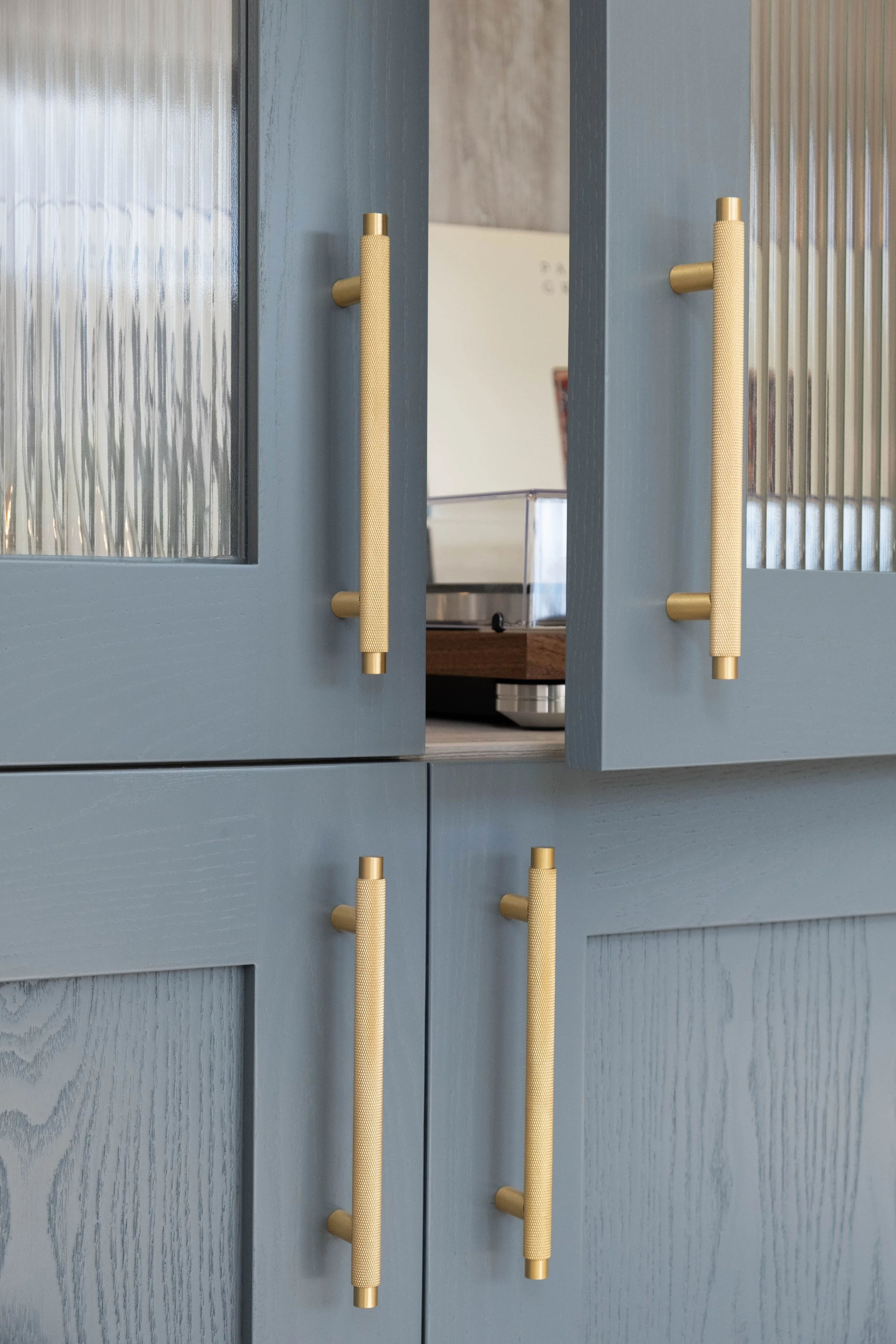 A pair of blue cabinet doors with textured glass panels and beige handles open to reveal a kitchen interior with a wooden countertop and a toaster.