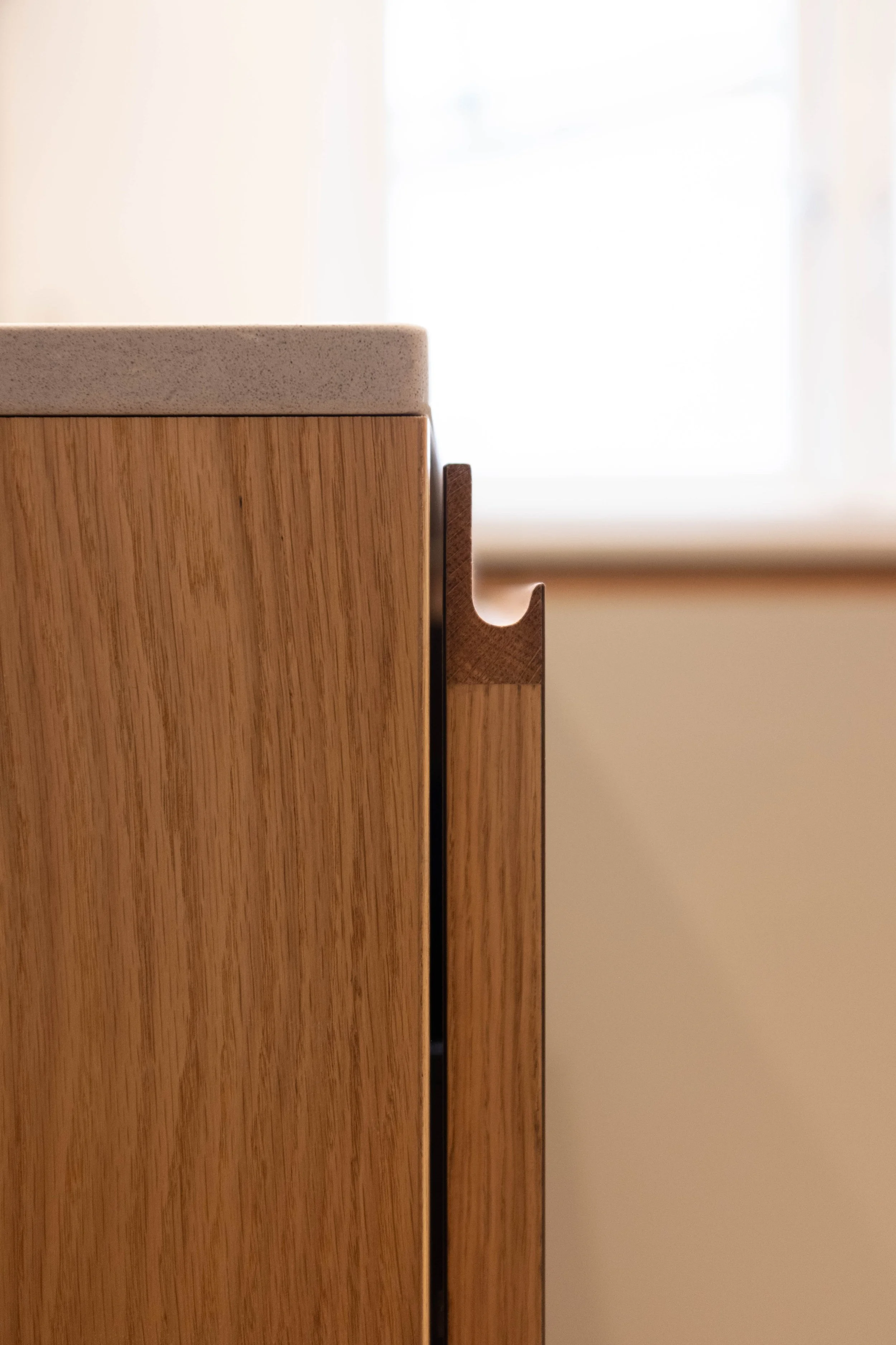 Close-up of a wooden cabinet with a light-colored countertop and a rich wood grain finish, against a bright window background.