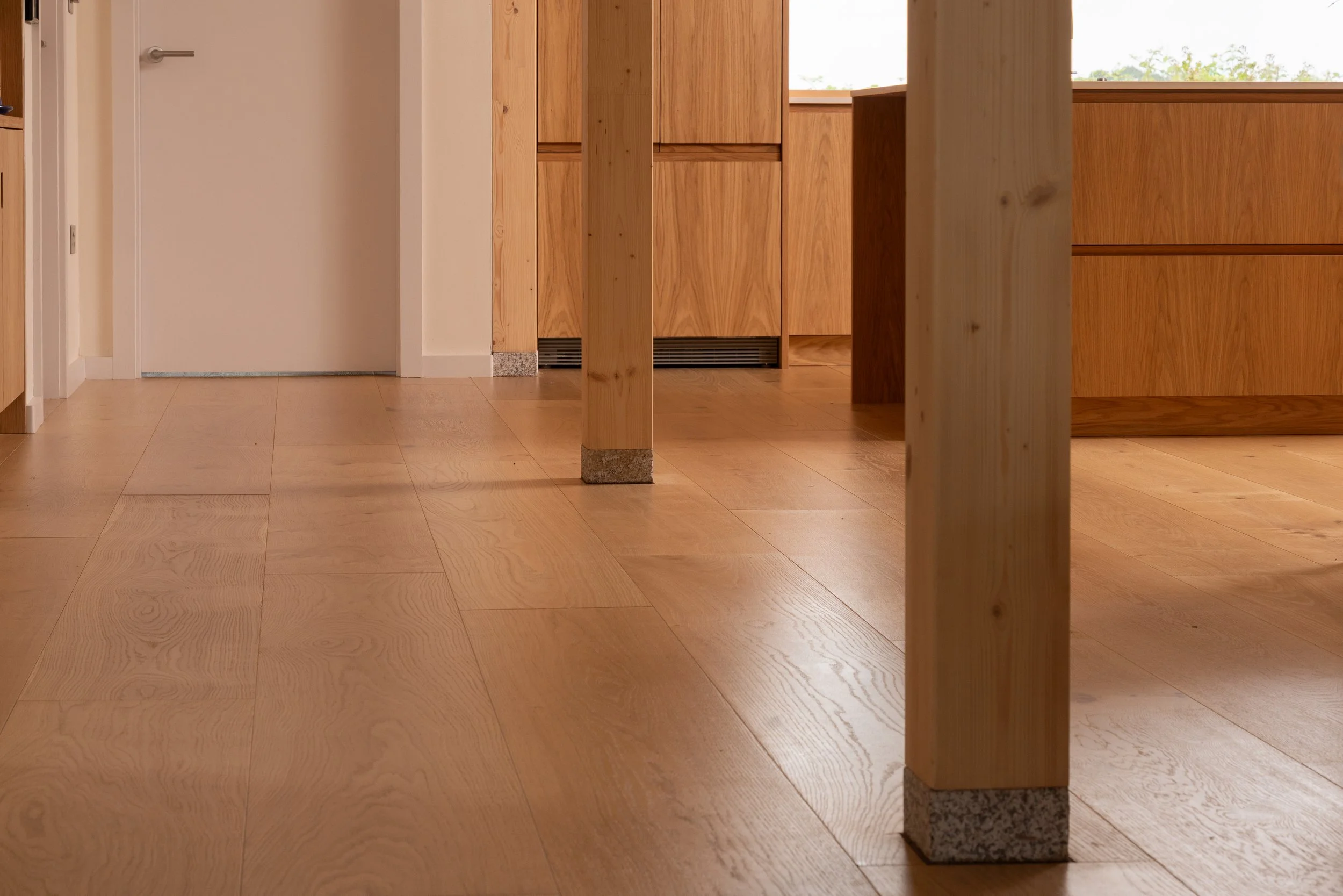 Interior view of a room with light-colored wooden flooring, wooden furniture, and a door in the background.