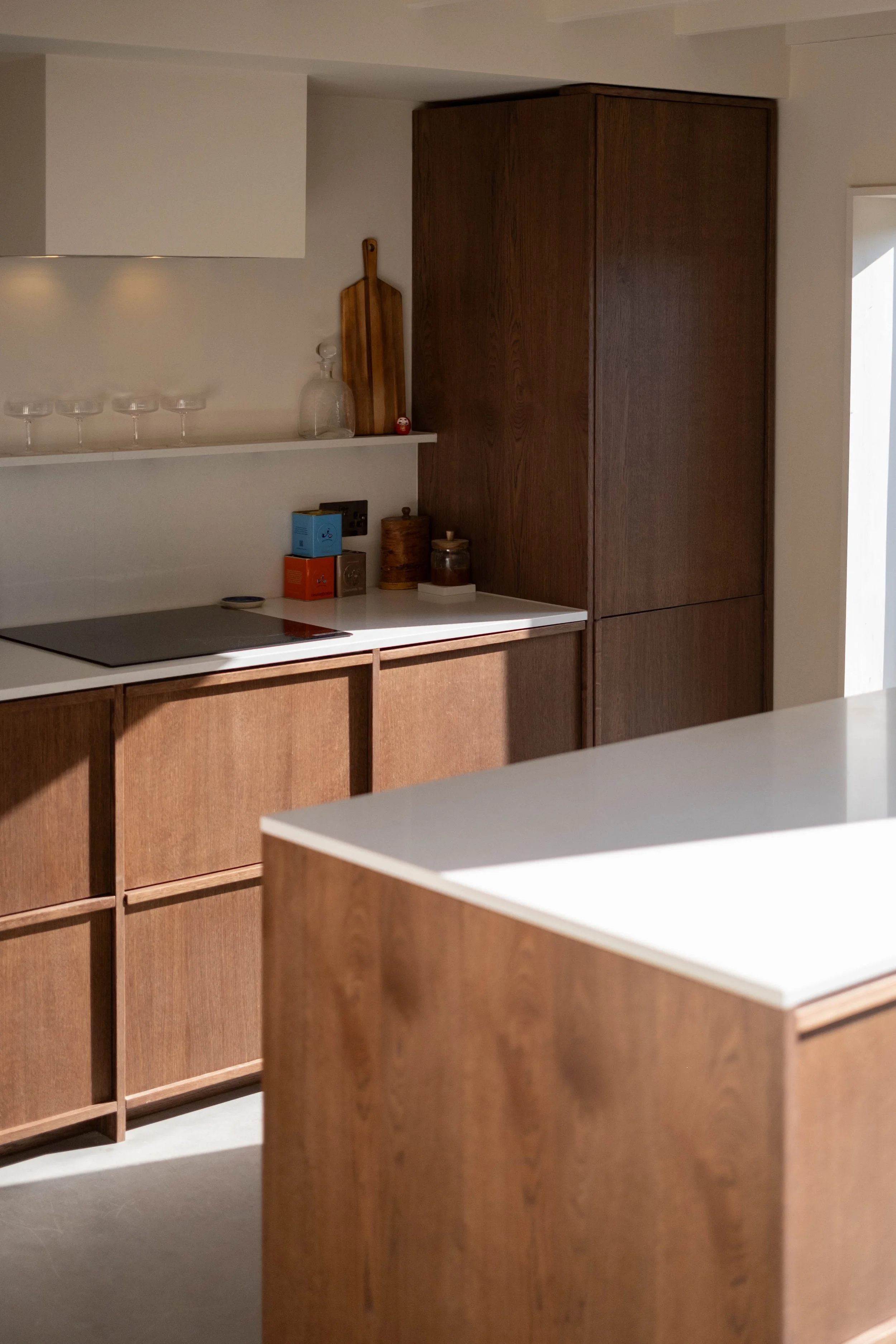 A kitchen with wooden cabinets, a white countertop, a black stovetop, and decorative items such as a glass jar, wooden cutting boards, and small boxes.