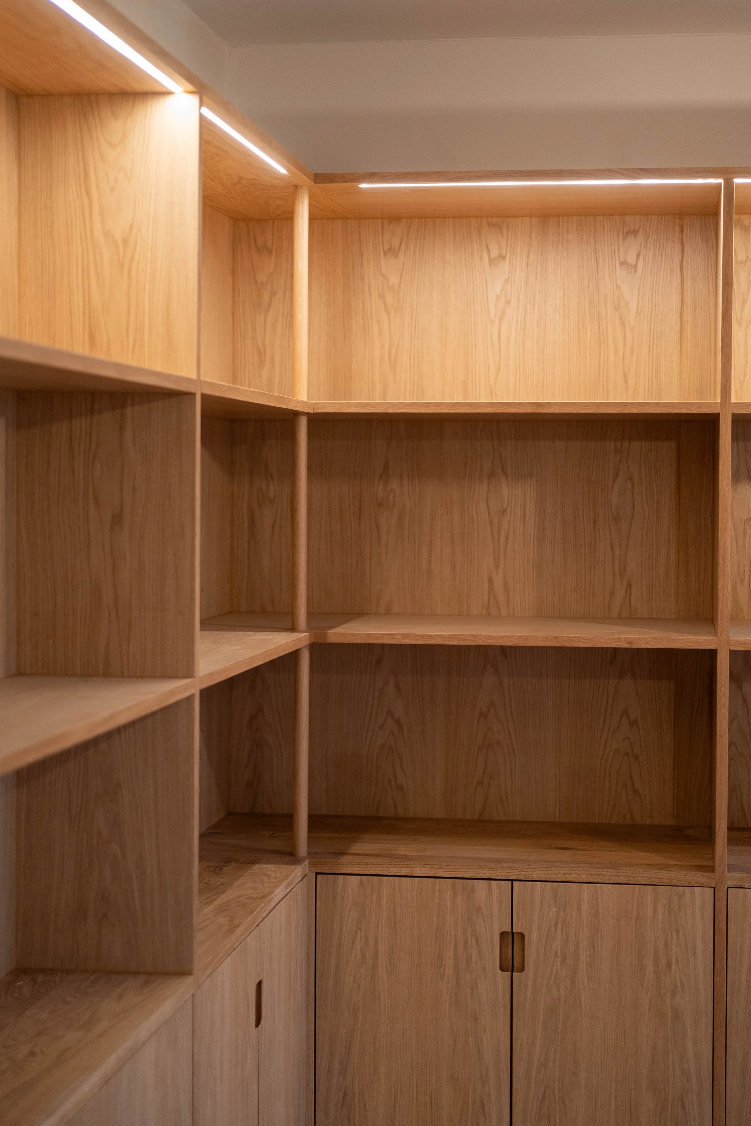 Empty wooden shelving unit with multiple compartments, including lower cabinet doors with cut-out handles.
