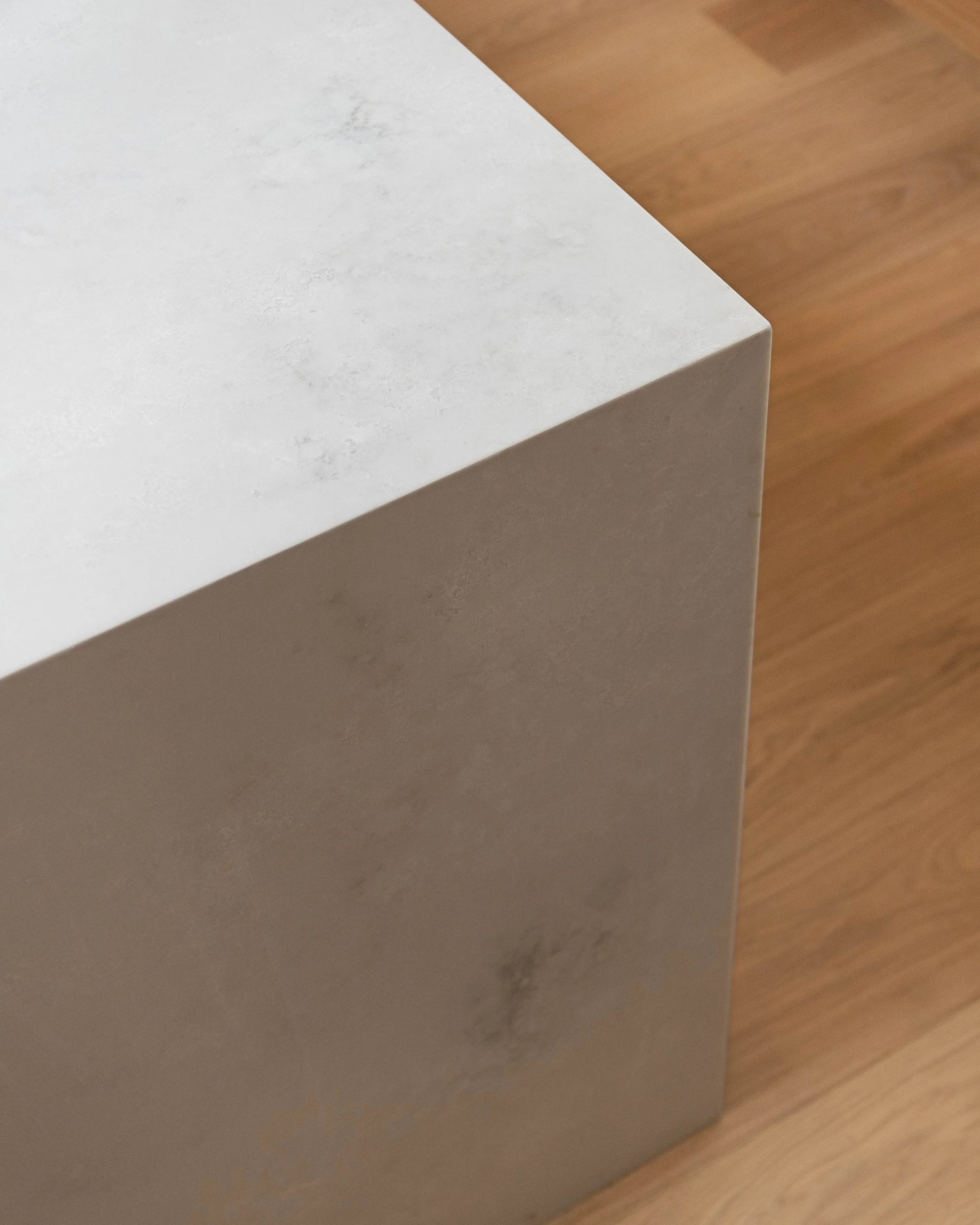 Close-up of a corner of a white marble table with a wooden floor underneath.