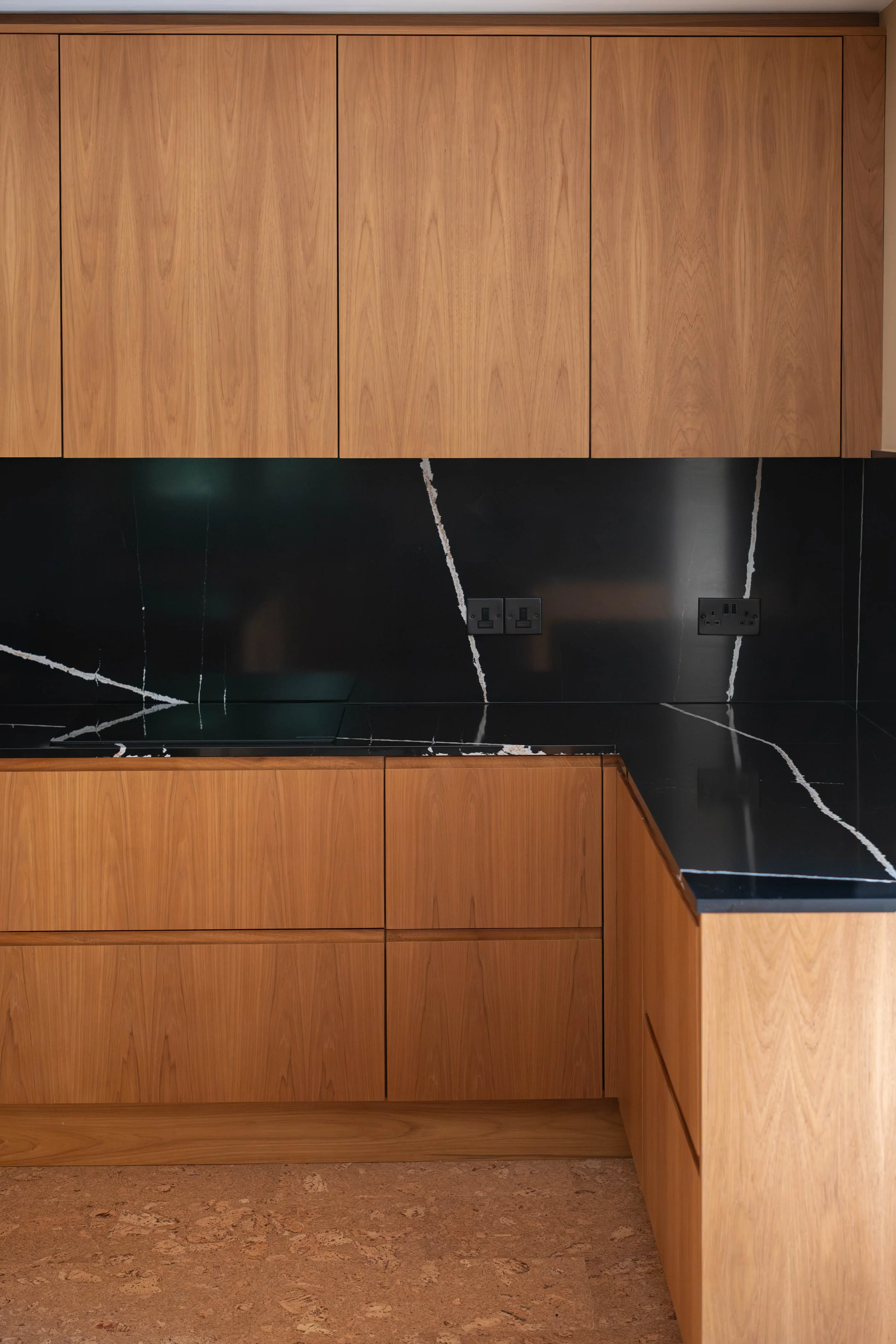 Close-up of a modern kitchen with black marble cabinets featuring white veining, wooden upper and lower cabinets, and electrical outlets.