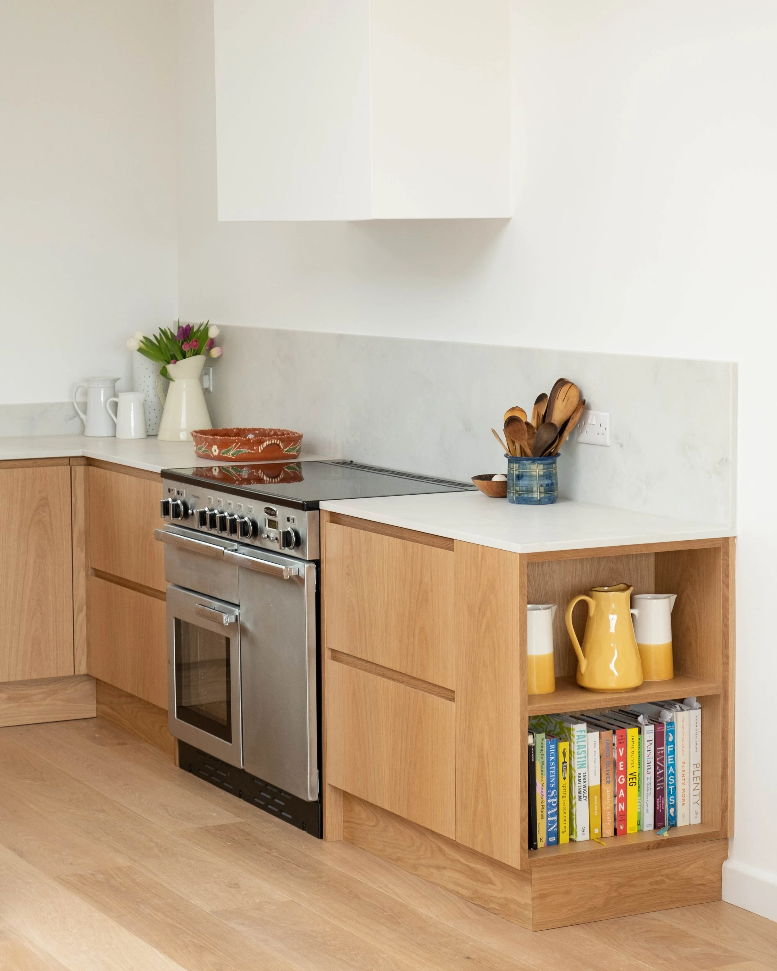 Modern kitchen with wooden cabinets, a stovetop with oven, yellow vases, and a bookshelf with cookbooks.