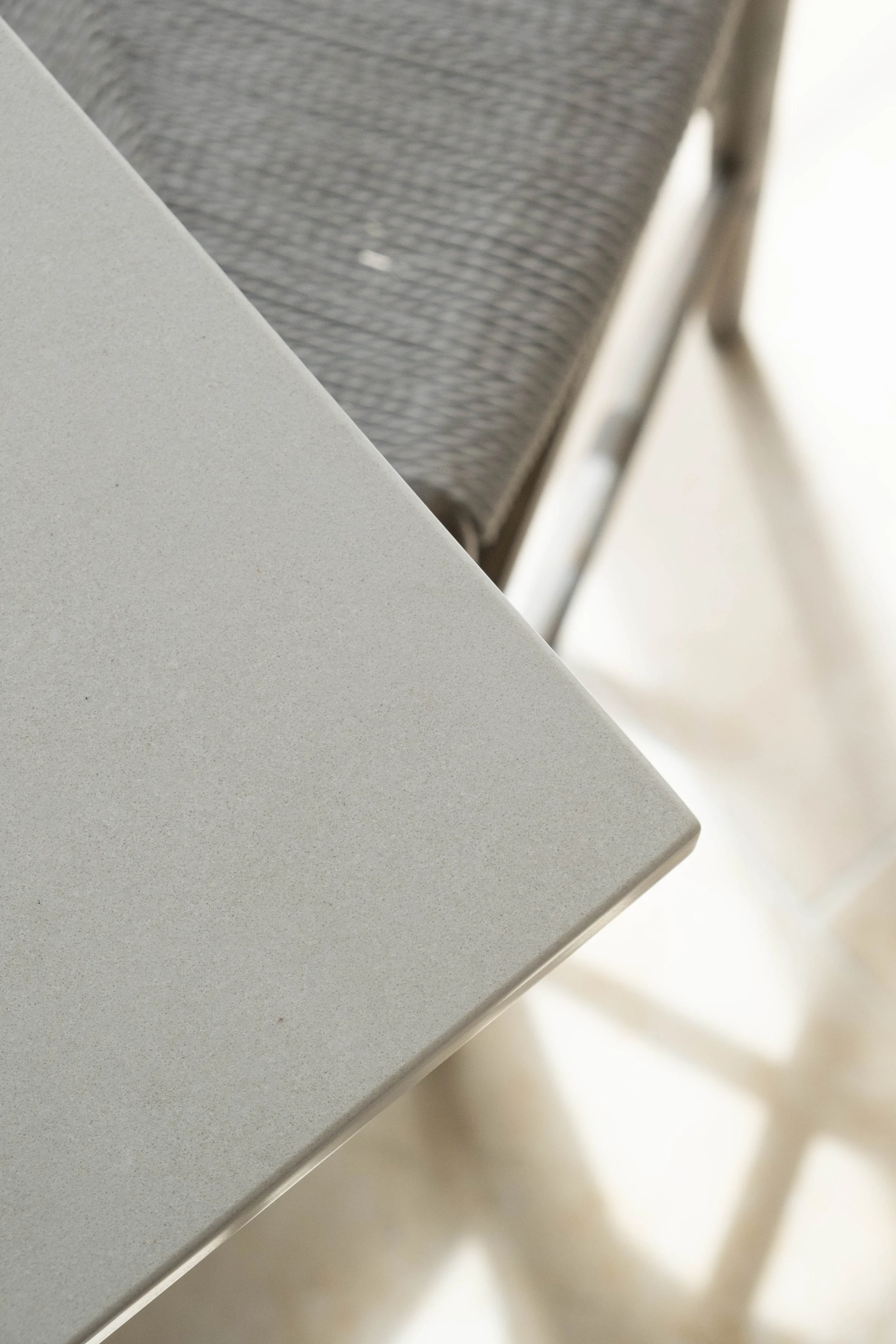 Close-up of a corner of a light gray table with a gray fabric chair in the background, partially out of focus.