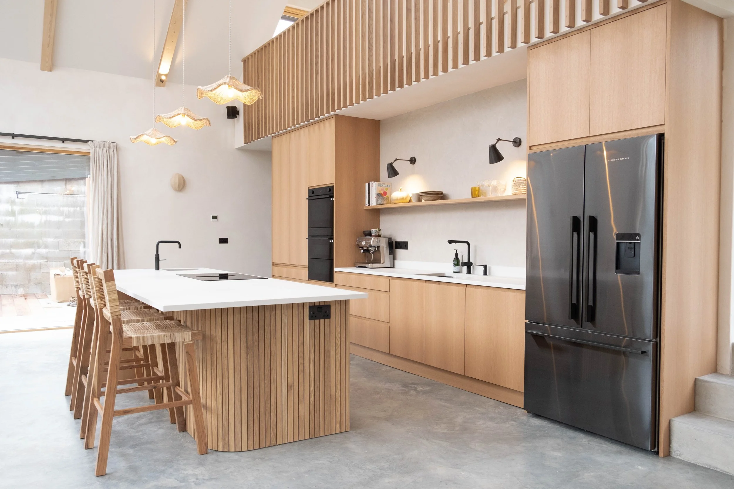Modern kitchen with wooden cabinetry, a large white kitchen island with bar stools, stainless steel appliances, and hanging pendant lights.