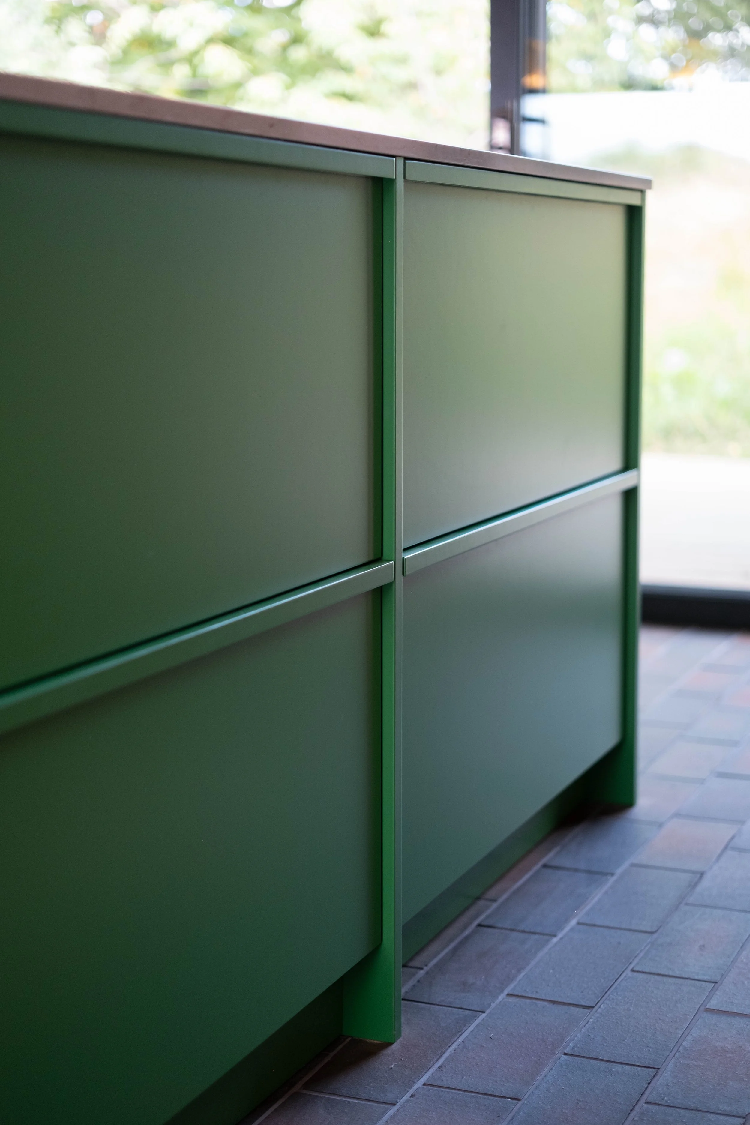 Close-up of a green cabinet with multiple drawers, situated against a window with a view of green trees outside.