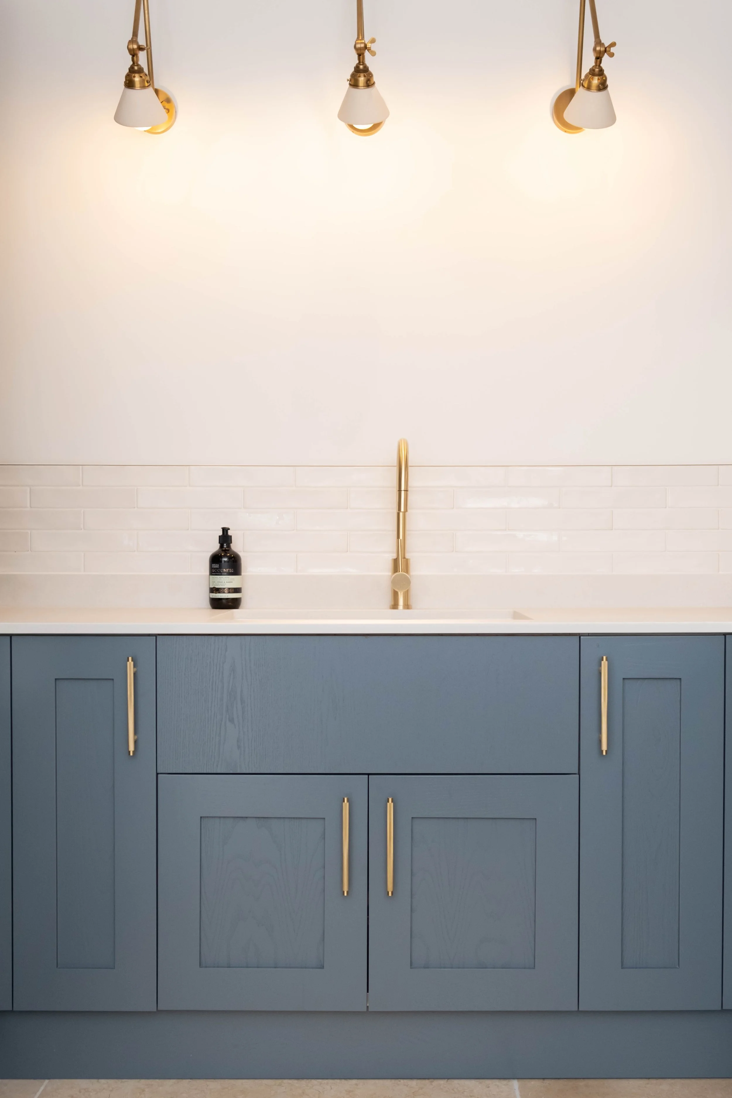Blue kitchen cabinet with gold handles, white countertop, gold faucet, and a black bottle of soap or lotion on the left side.