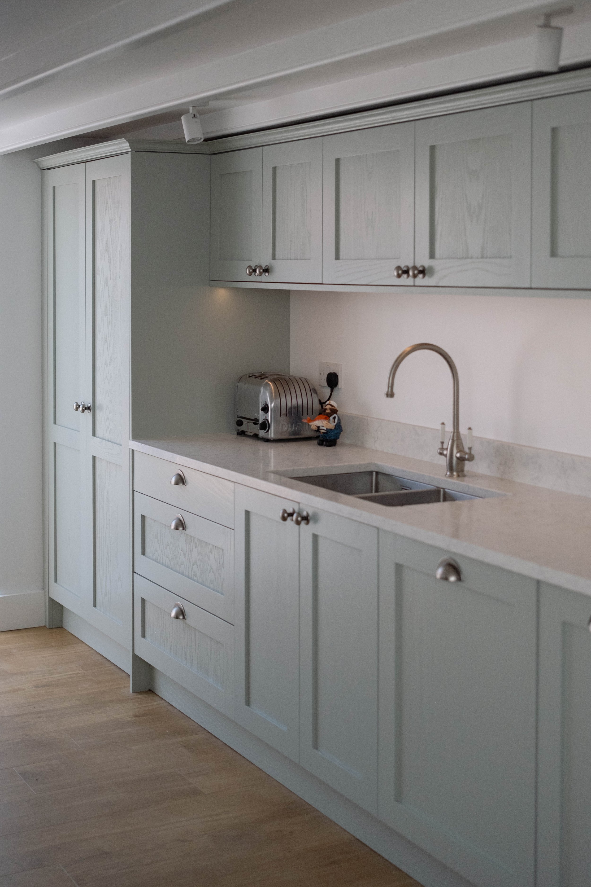 A kitchen with white wooden cabinets, a marble countertop, a stainless steel toaster, a small figure of a cartoon character, and a stainless steel faucet over a sink.
