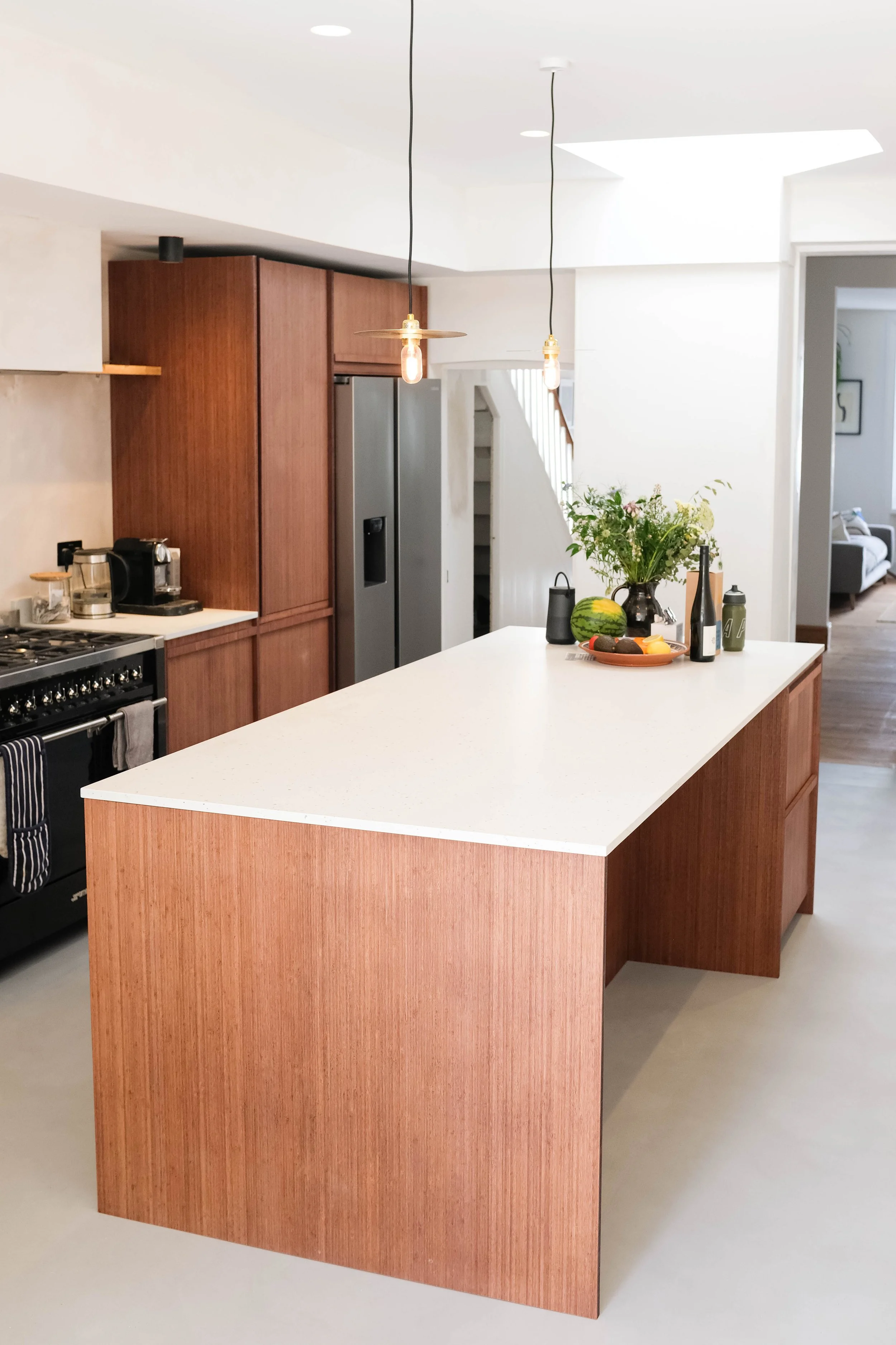 Modern kitchen with a white countertop island, wooden cabinets, stainless steel appliances, a vase with flowers, and pendant lights hanging from the ceiling.