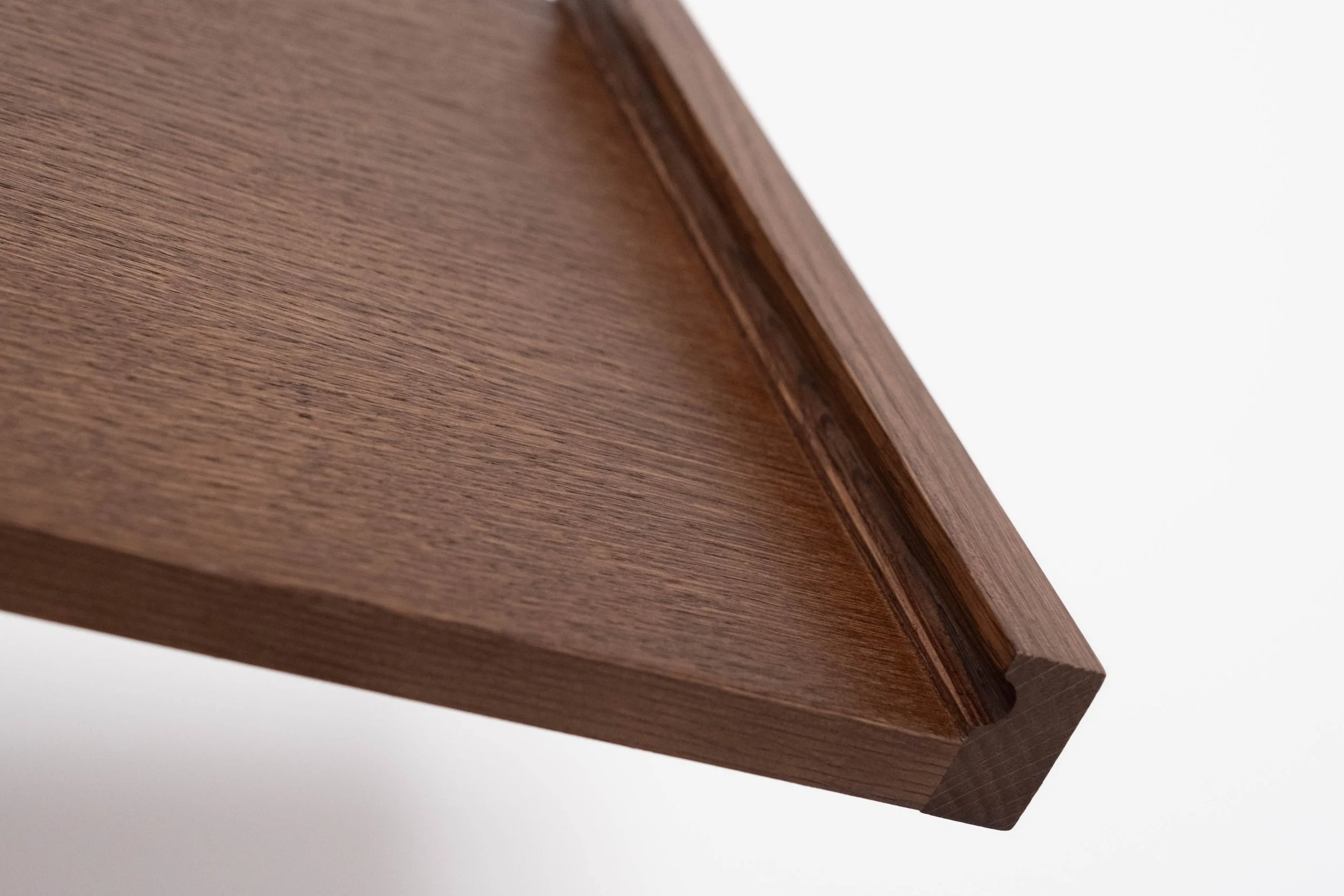 Close-up of a wooden piece with a smooth finish and visible wood grain, possibly part of furniture, against a plain white background.