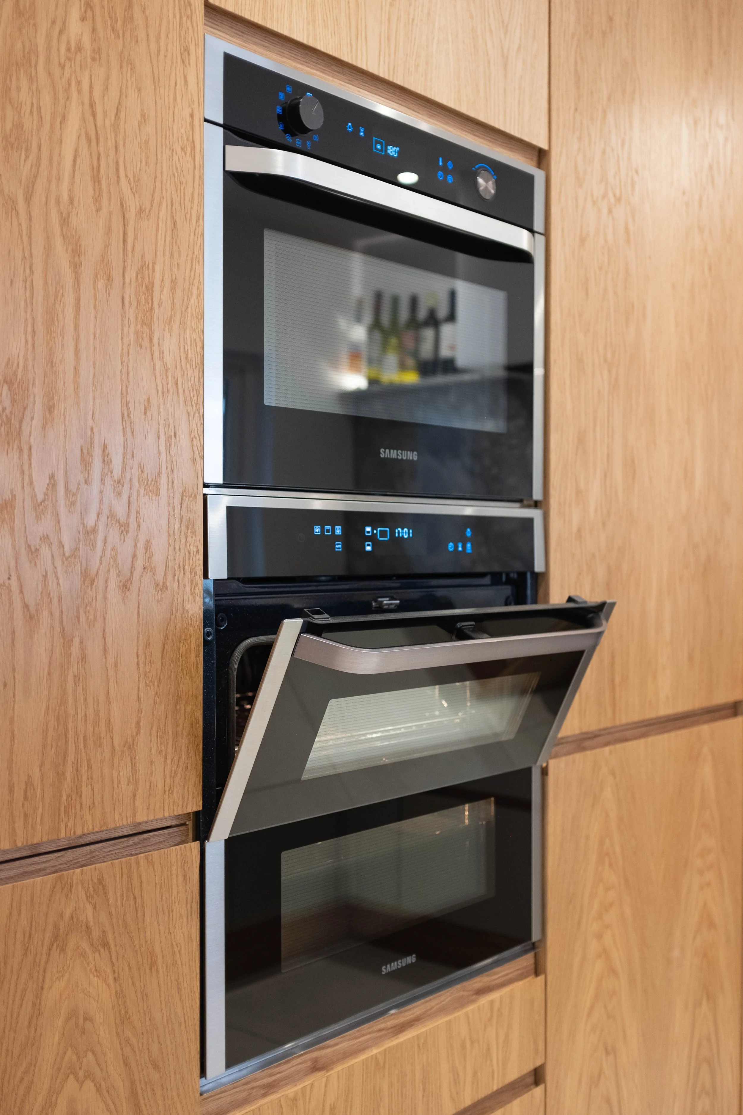 A modern built-in oven with a black and stainless steel finish, digital controls, and a glass door, built into wooden kitchen cabinetry.