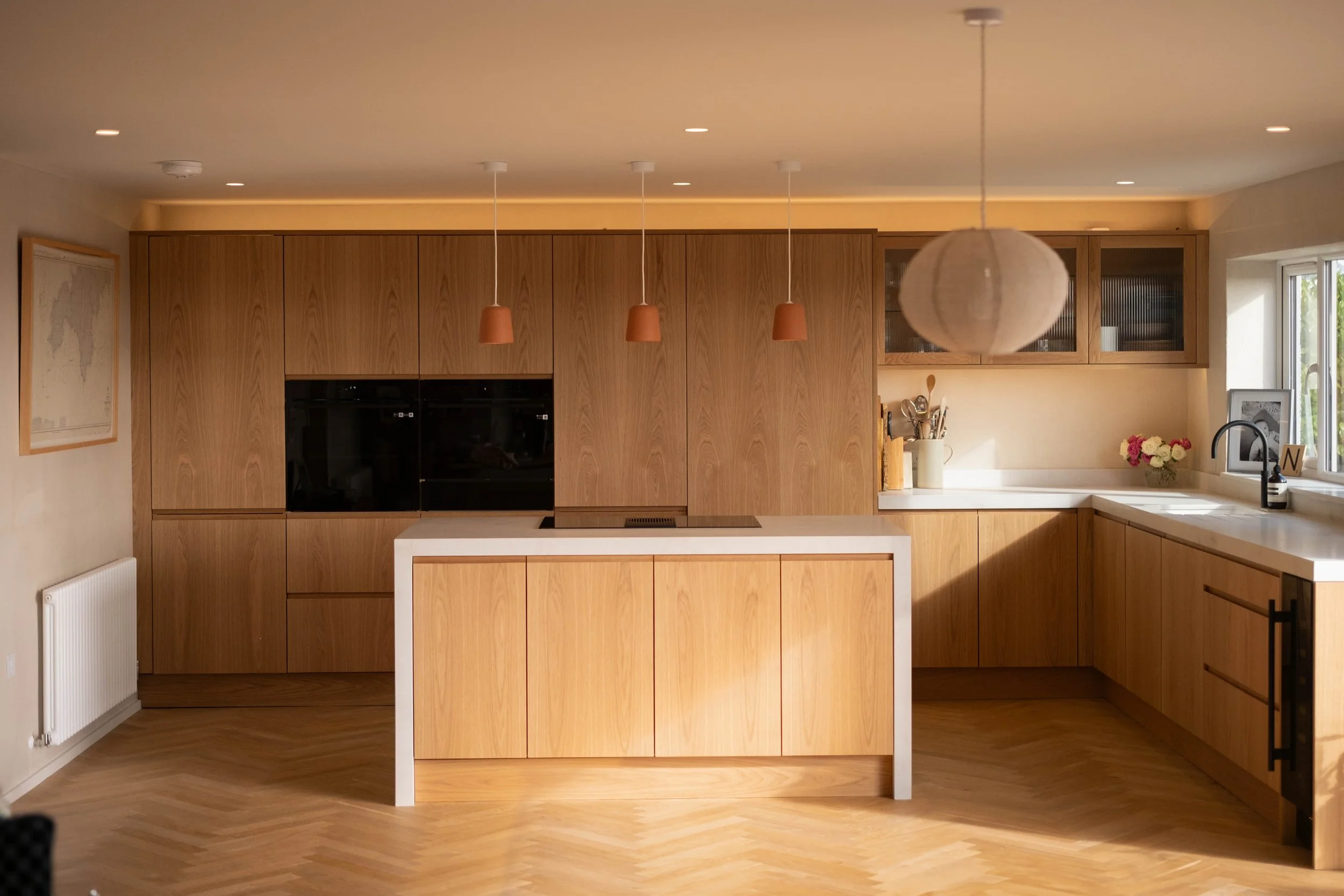 Modern kitchen with wooden cabinets, white island, pendant lights, and a window with a flower vase and framed picture on the countertop.