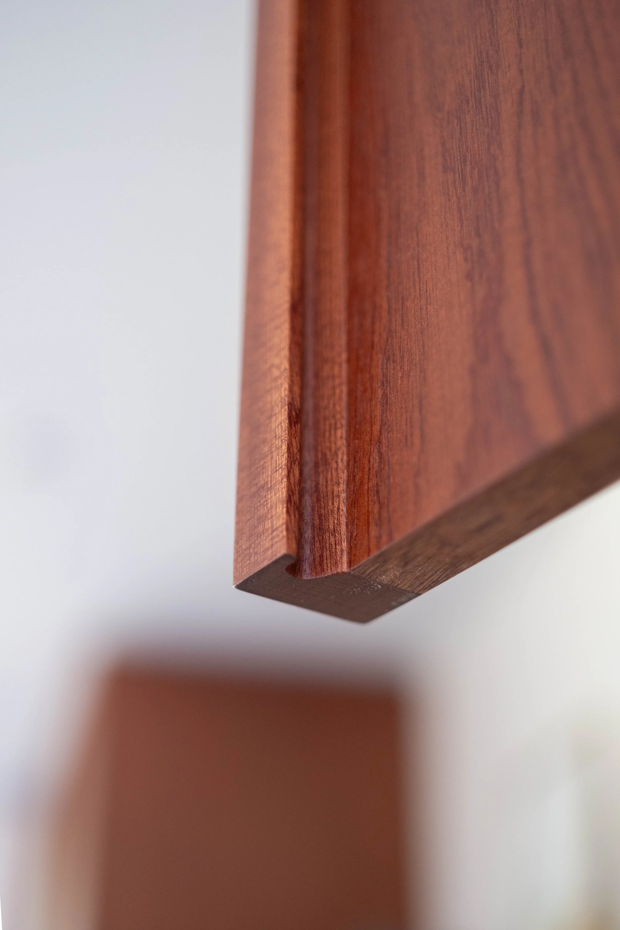 Close-up of a wooden surface, possibly furniture, with a smooth finish and visible wood grain. The image is taken at an angle showing the edge and a blurred background.