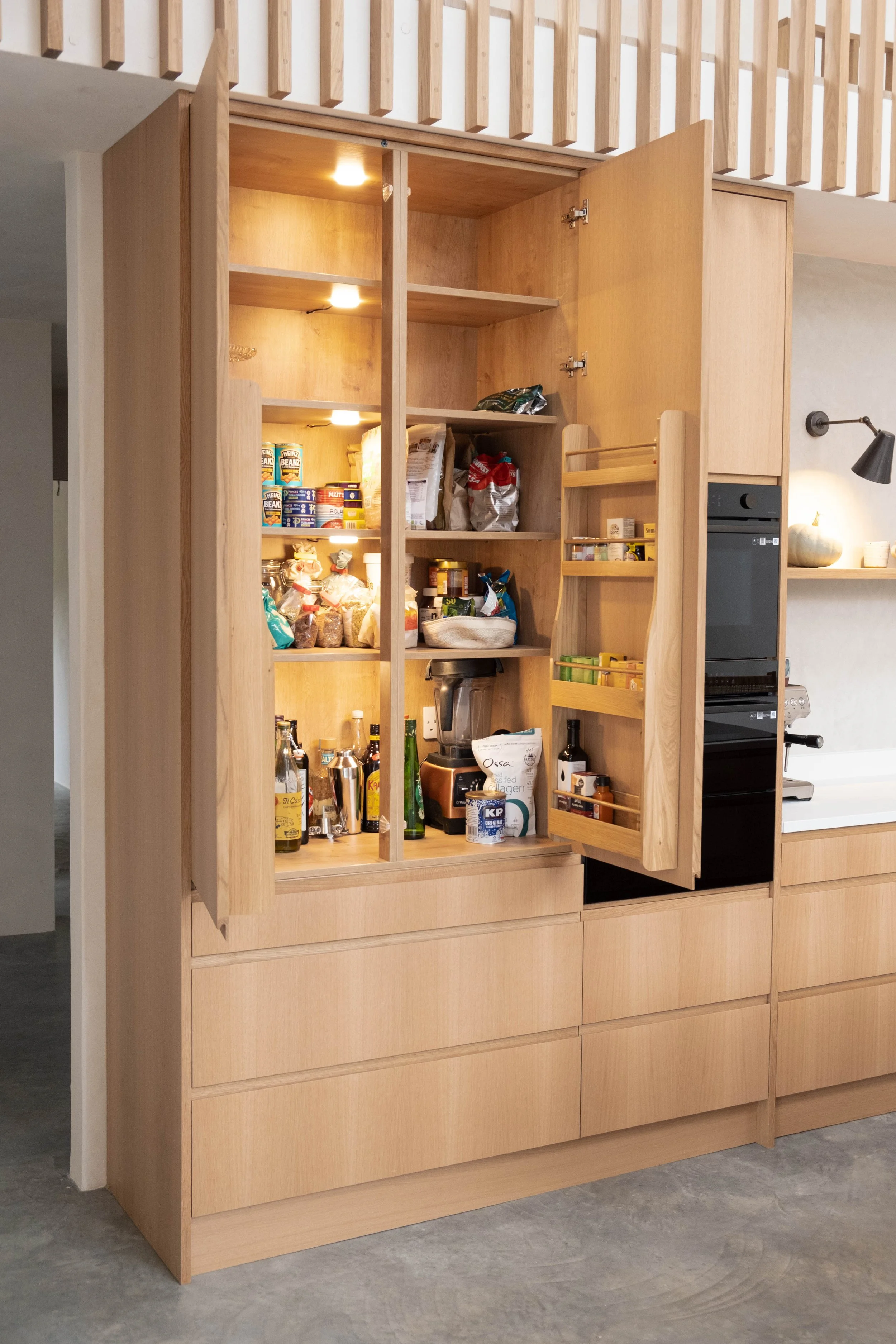 A large wooden kitchen cabinet with open doors revealing shelves with food items and kitchen supplies, with additional closed drawers below, in a modern kitchen setting.
