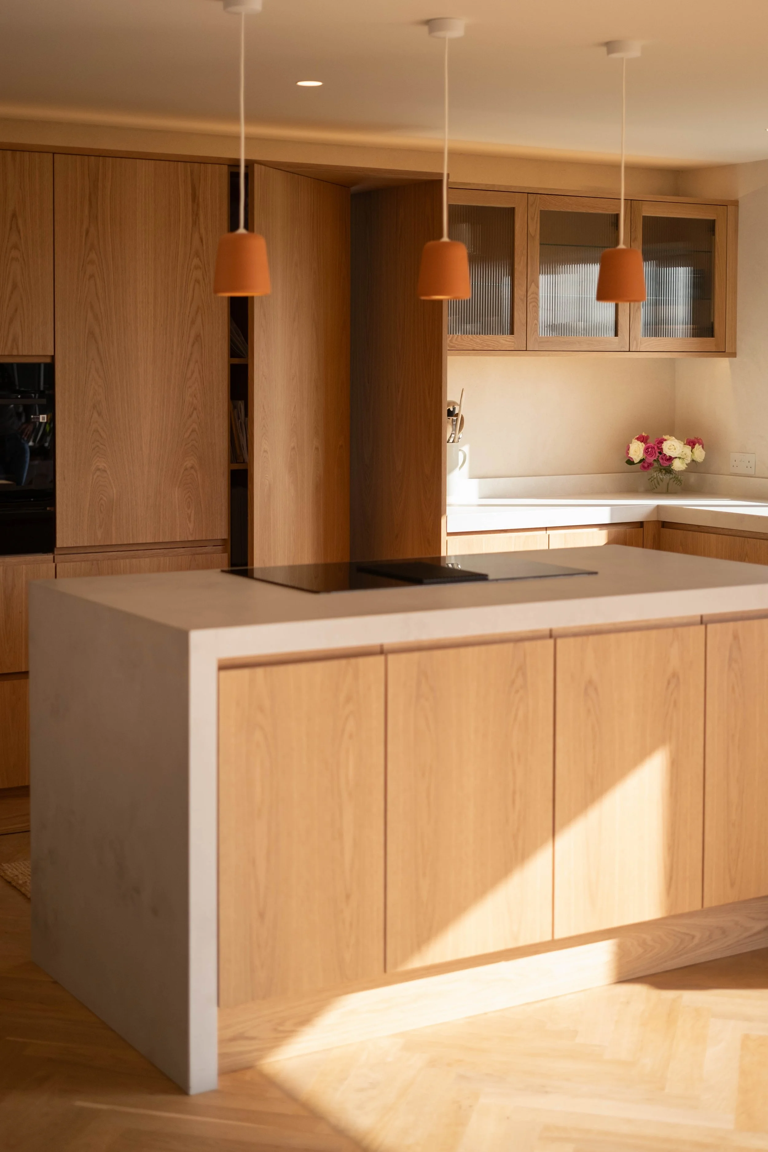 Modern kitchen with wooden cabinets, a white countertop, and three terracotta pendant lights hanging from the ceiling.
