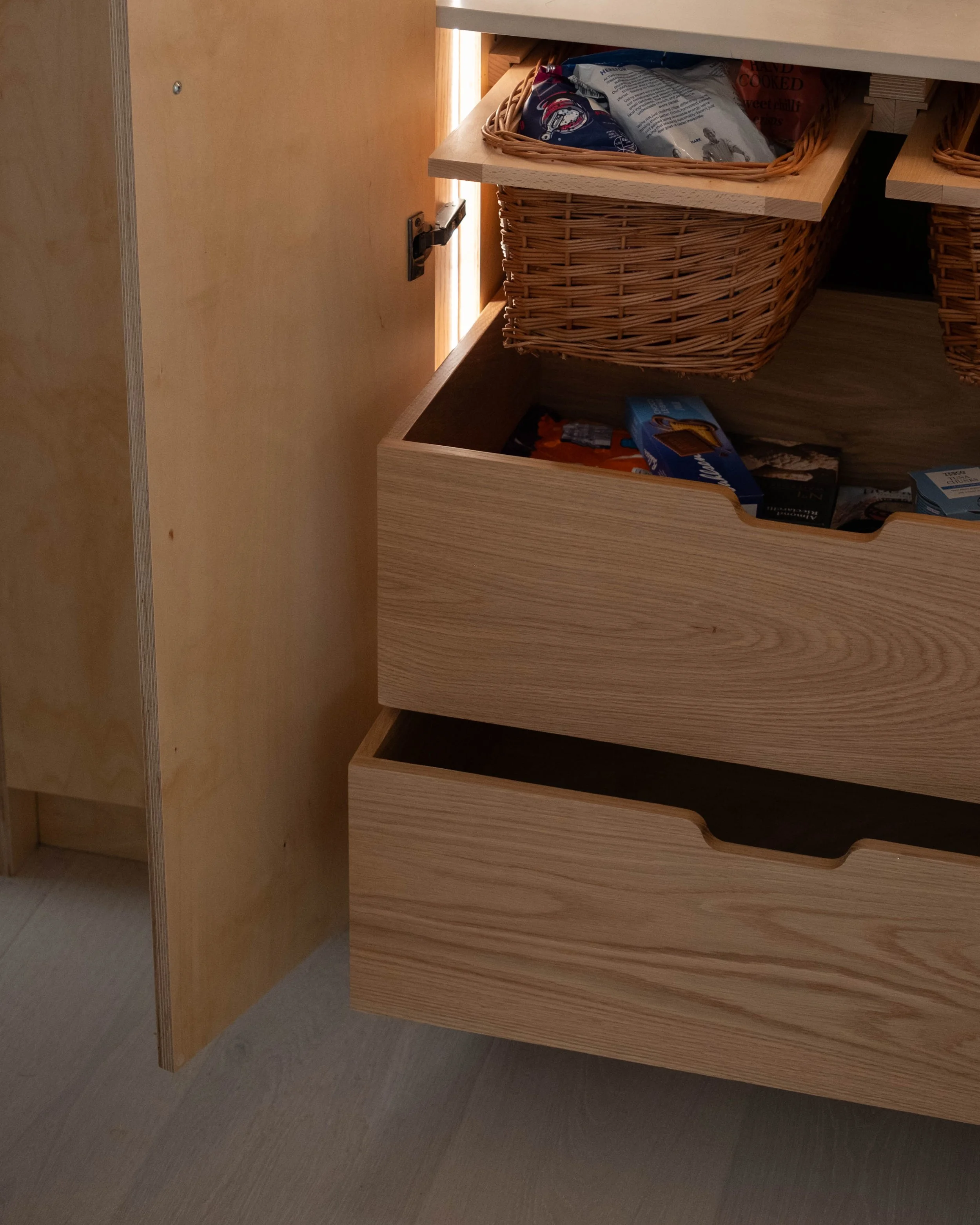 Open kitchen drawer with wooden and wicker baskets containing food items.
