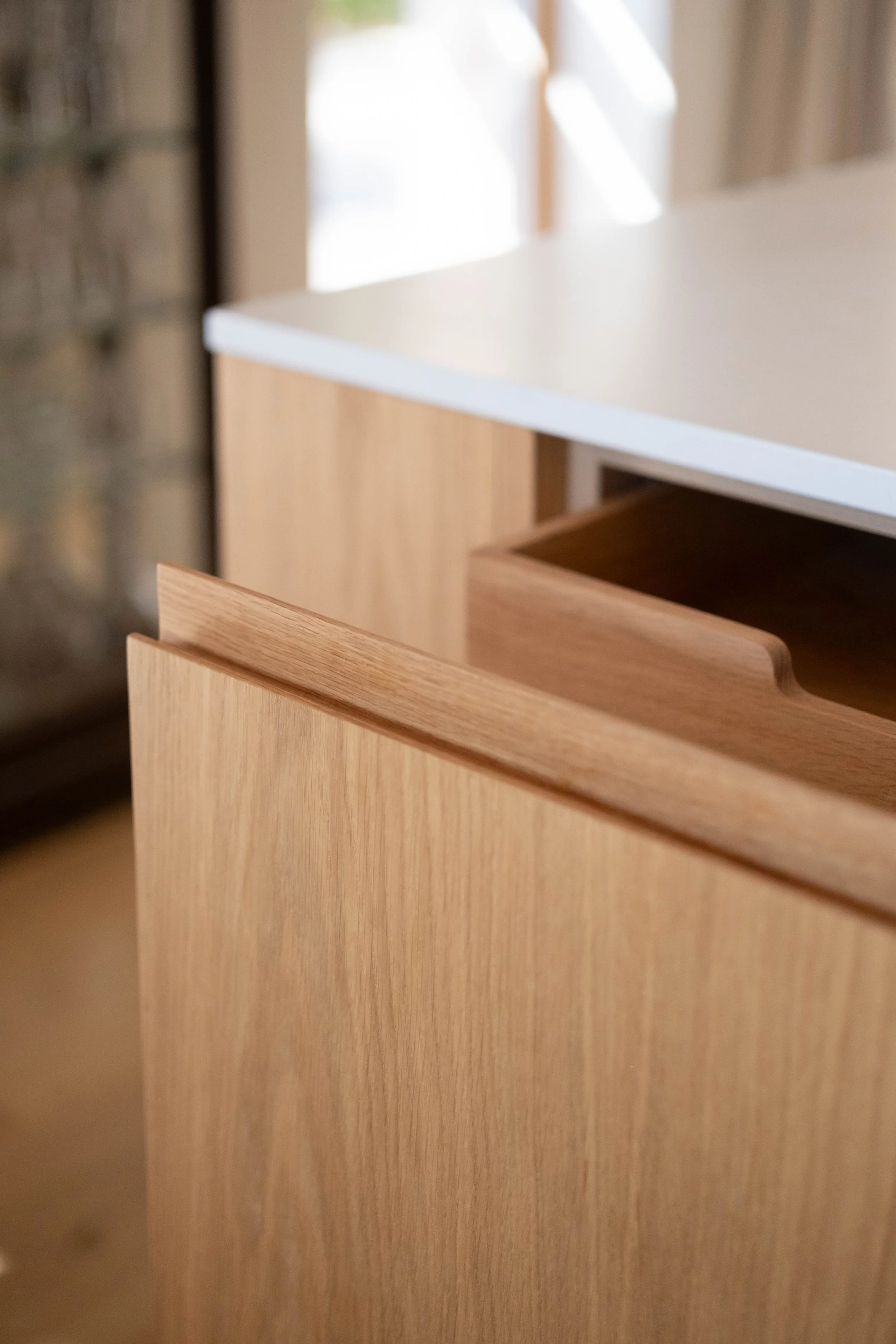 Close-up of a wooden drawer partially open, with a white countertop and beige wall in the background.
