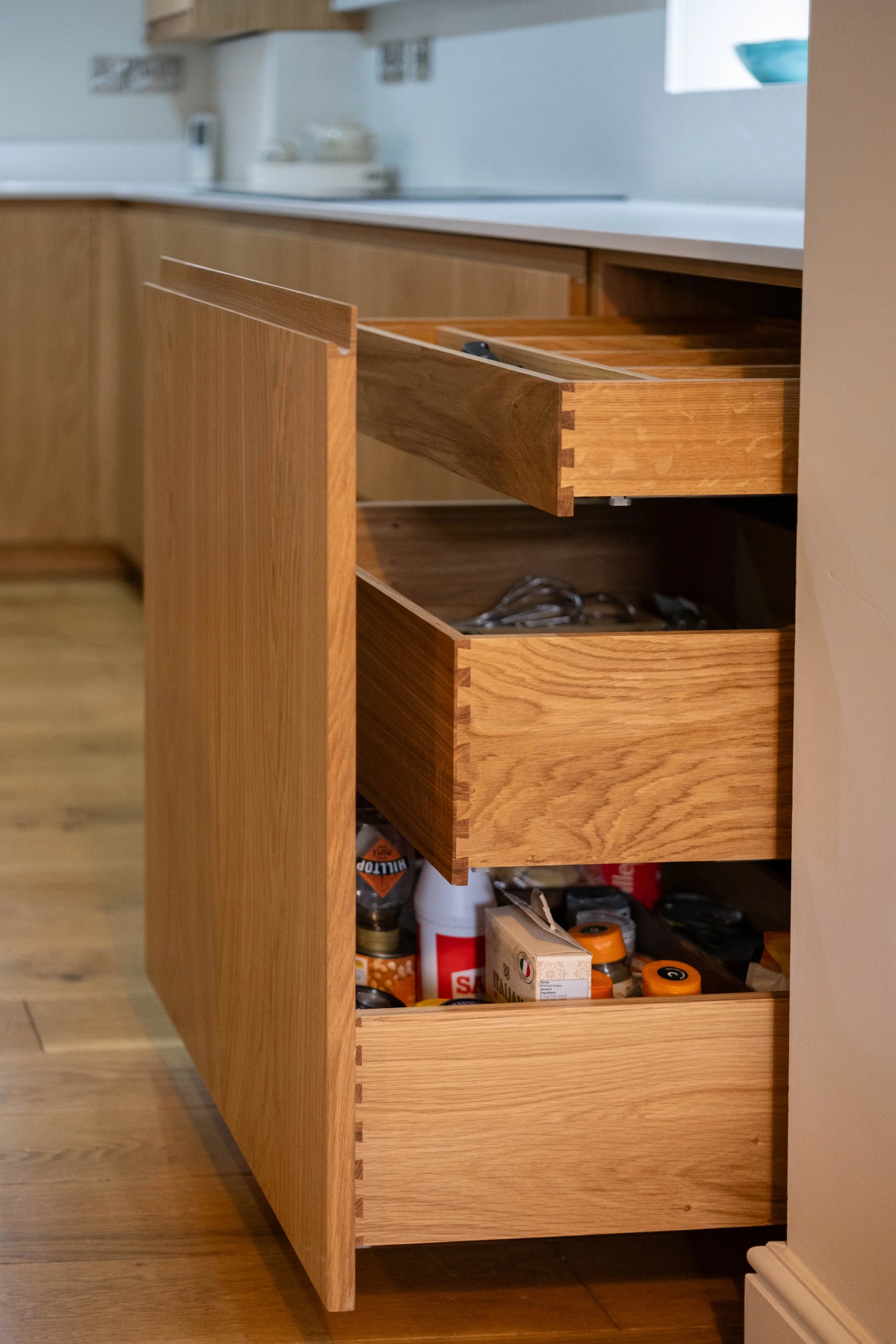 Open kitchen cabinet with wooden drawers and visible contents including jars, boxes, and kitchen supplies.