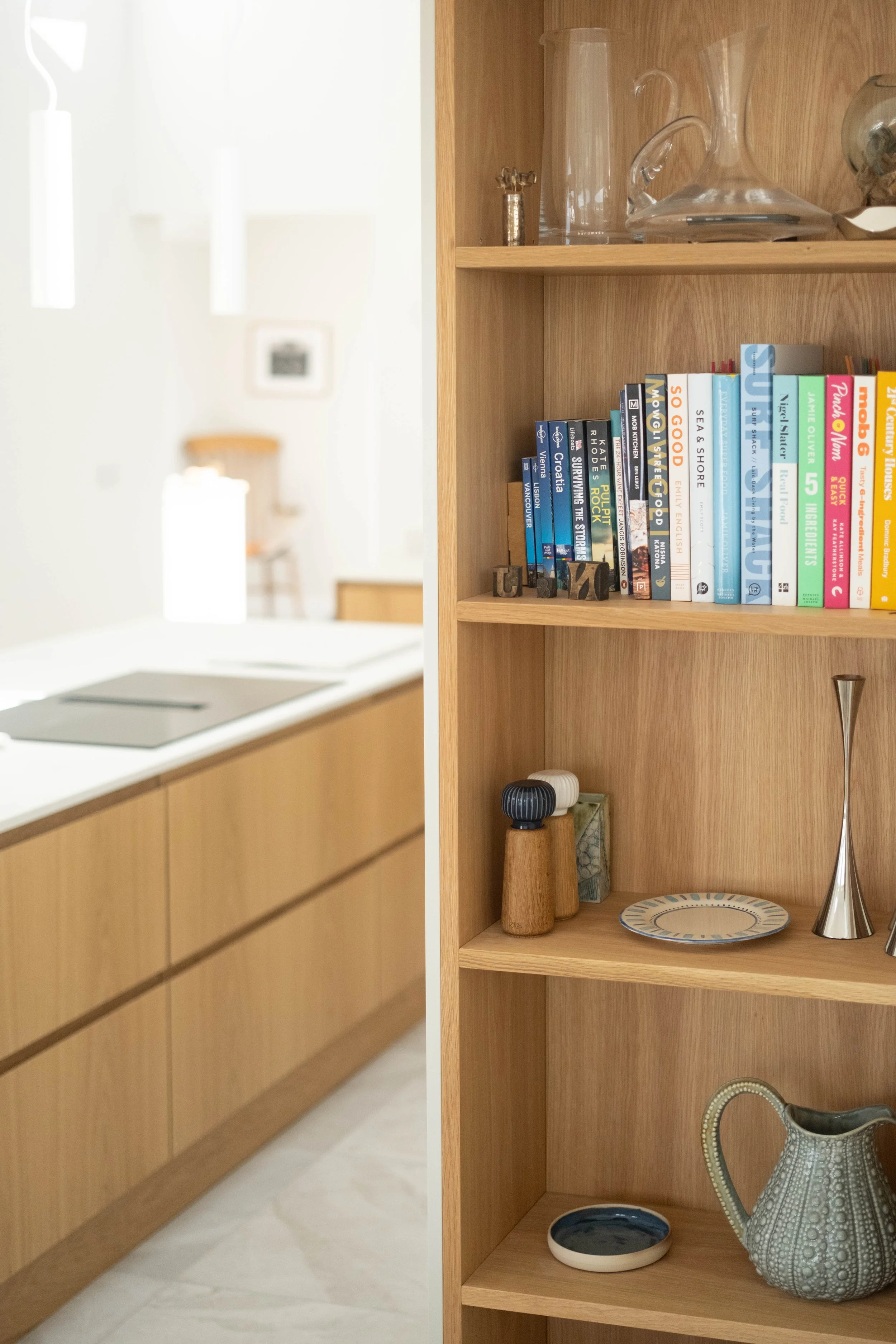 A close-up of a wooden bookshelf with decorative items and books, adjacent to a kitchen countertop with a stove and wooden cabinets in a modern kitchen.