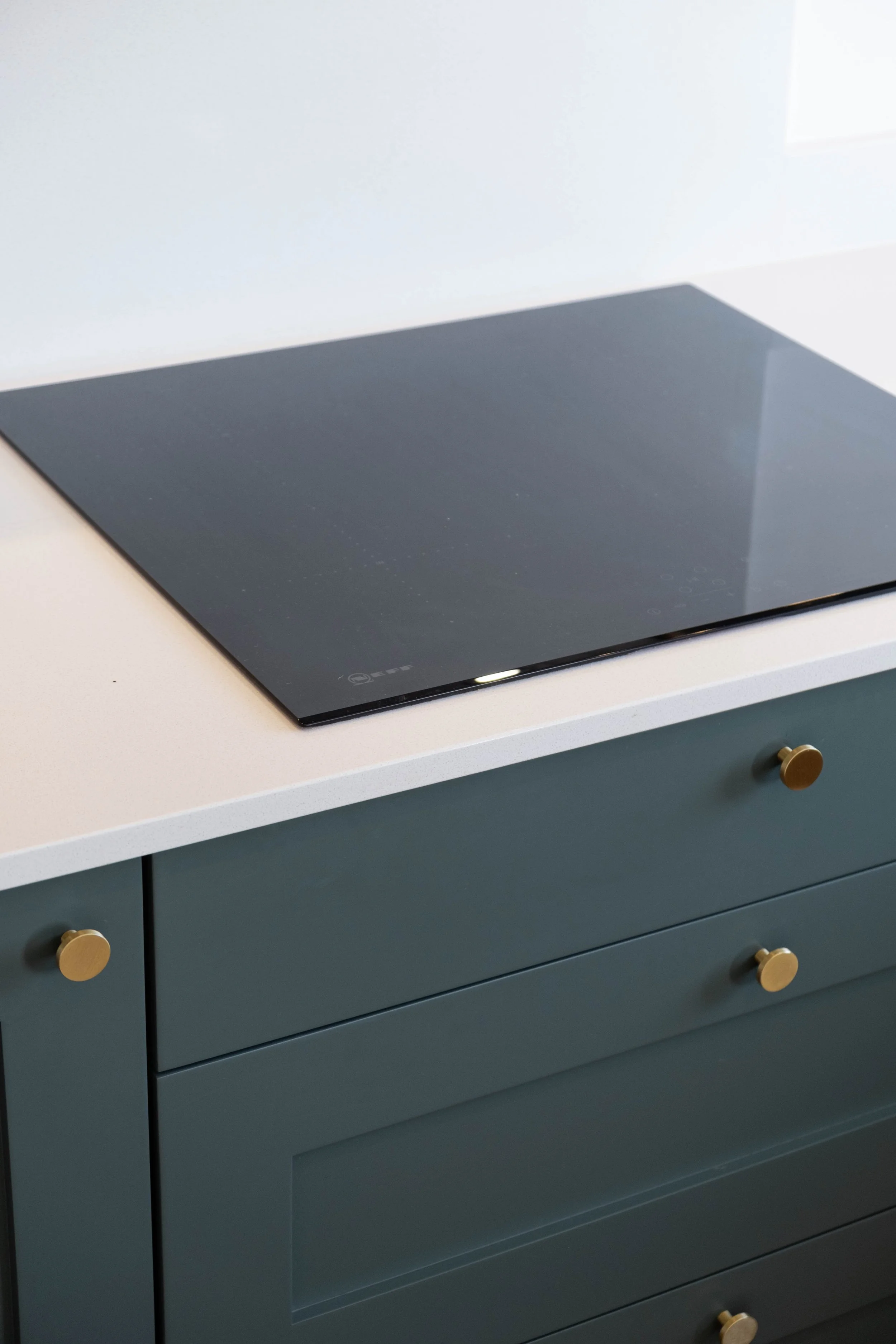 A kitchen stove with a black glass cooktop on a blue cabinet with round, gold knobs.