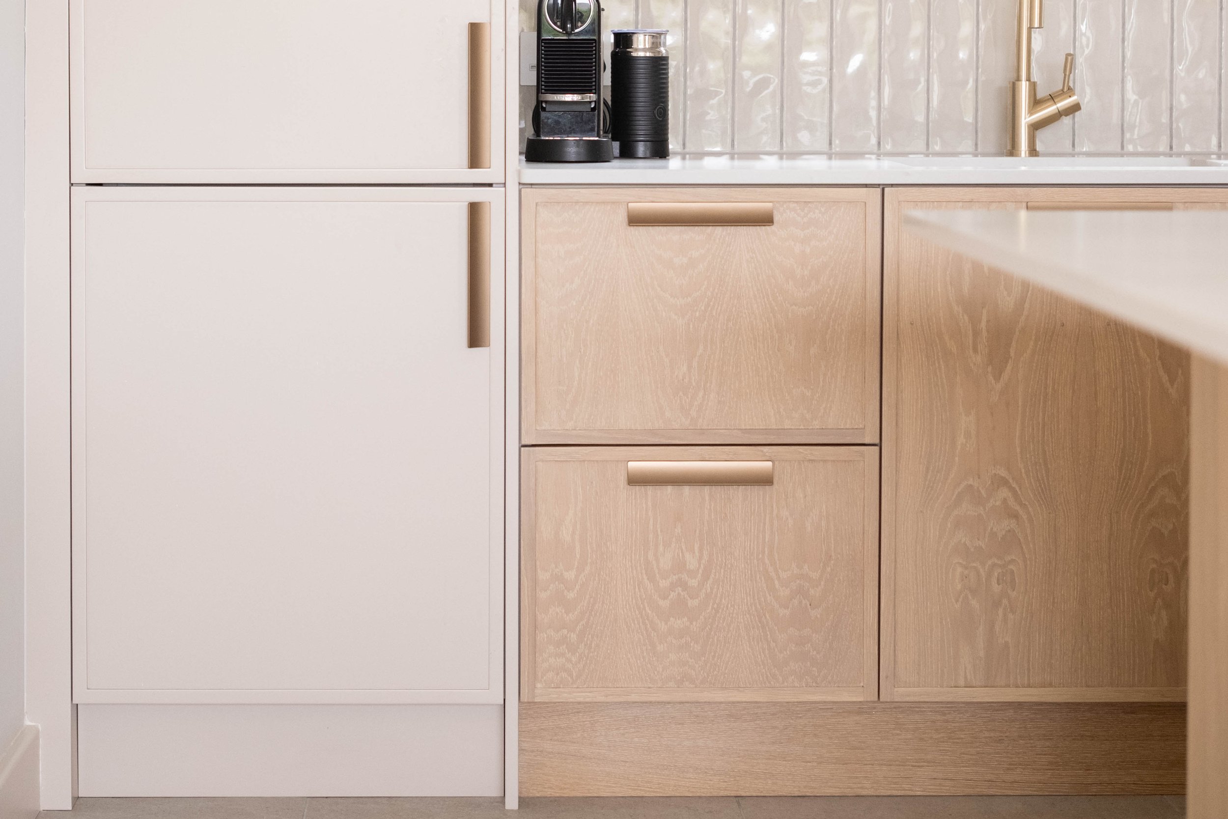 Kitchen cabinets with a white upper cabinet and light wood lower cabinet, displaying a coffee machine and a black thermal carafe on the countertop.