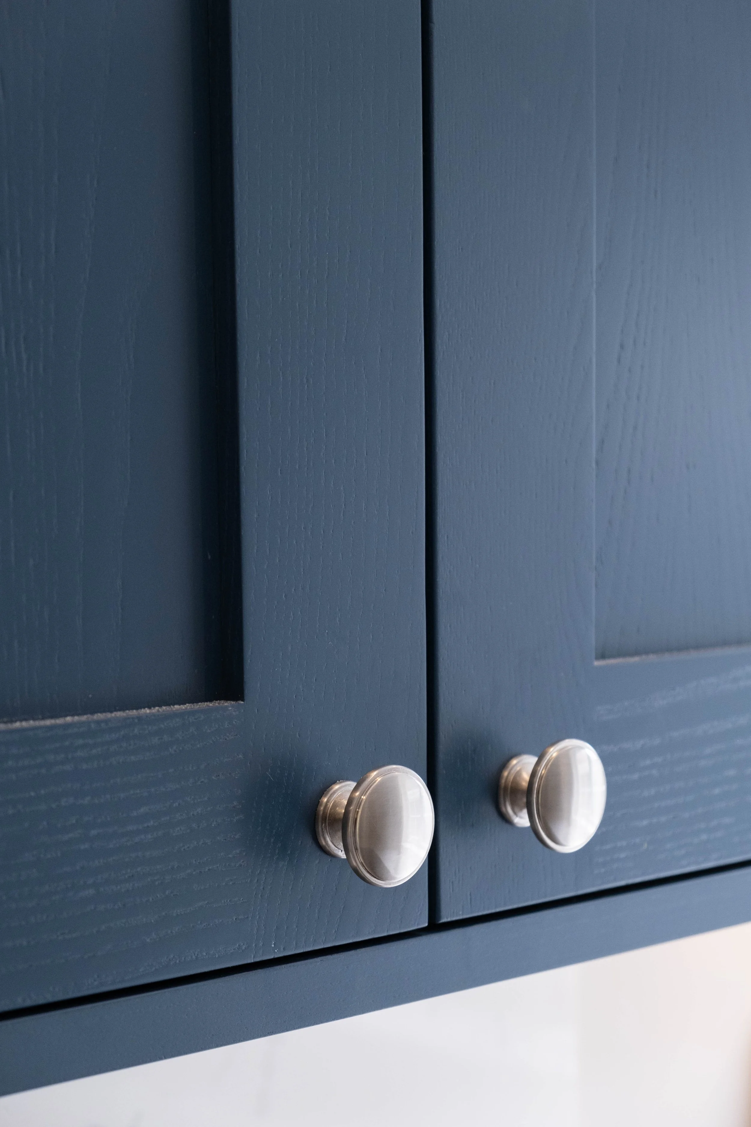 Close-up of dark blue kitchen cabinet doors with round silver knobs.