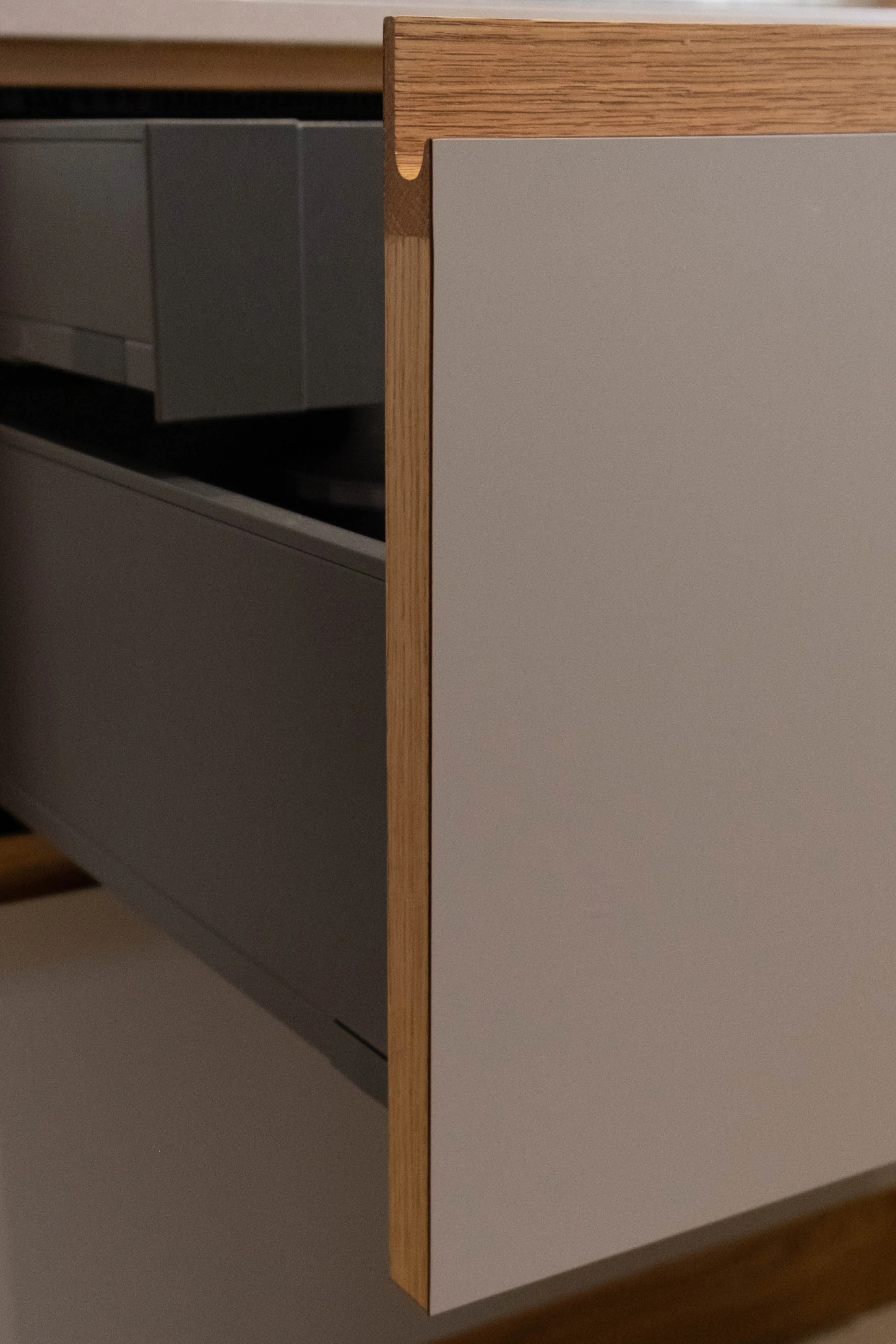 Close-up of a wooden and white cabinet with a smooth surface, partially open showing drawers inside, in a modern kitchen.