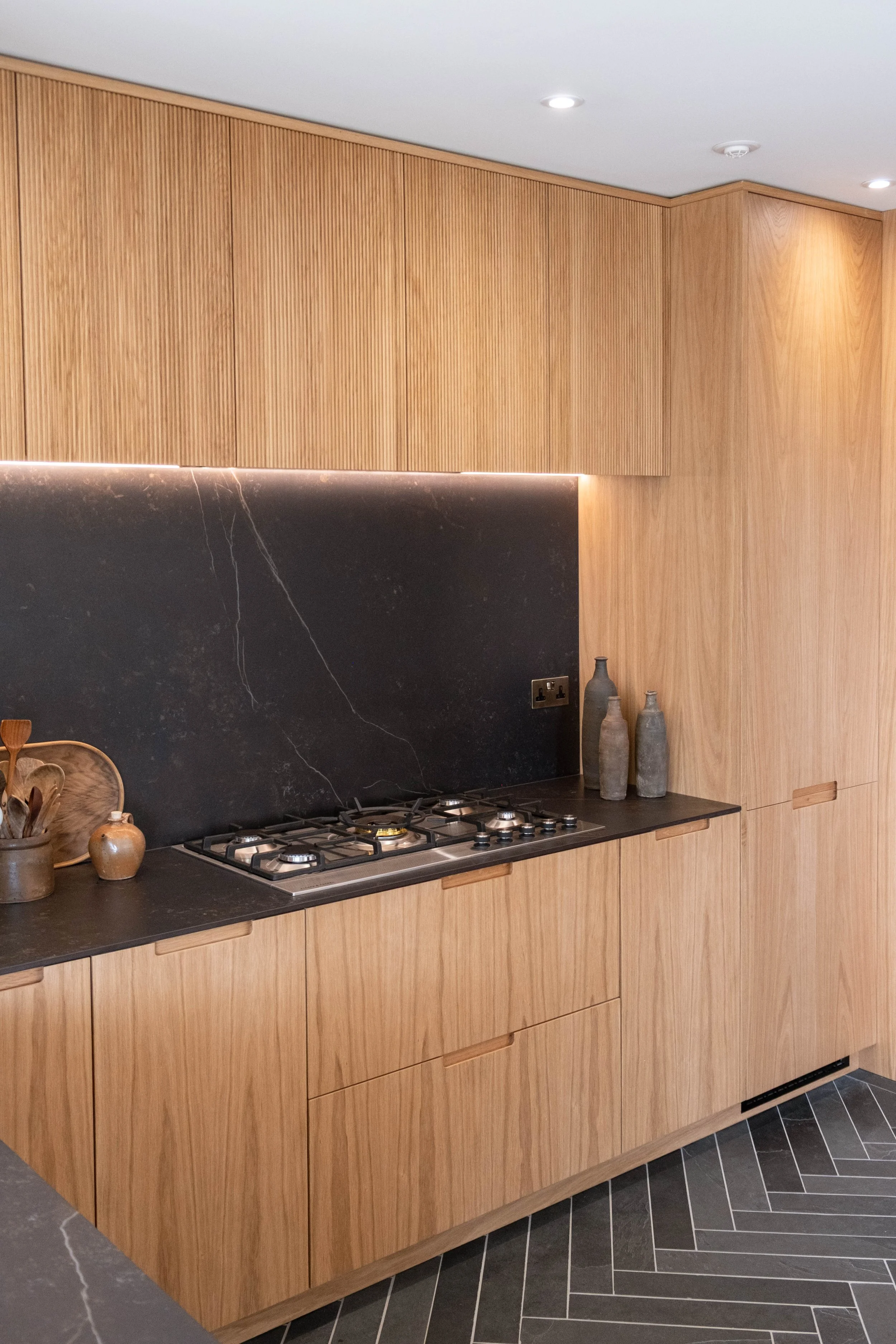 Modern kitchen with wooden cabinetry, black marble backsplash, gas stove, and decorative vases.