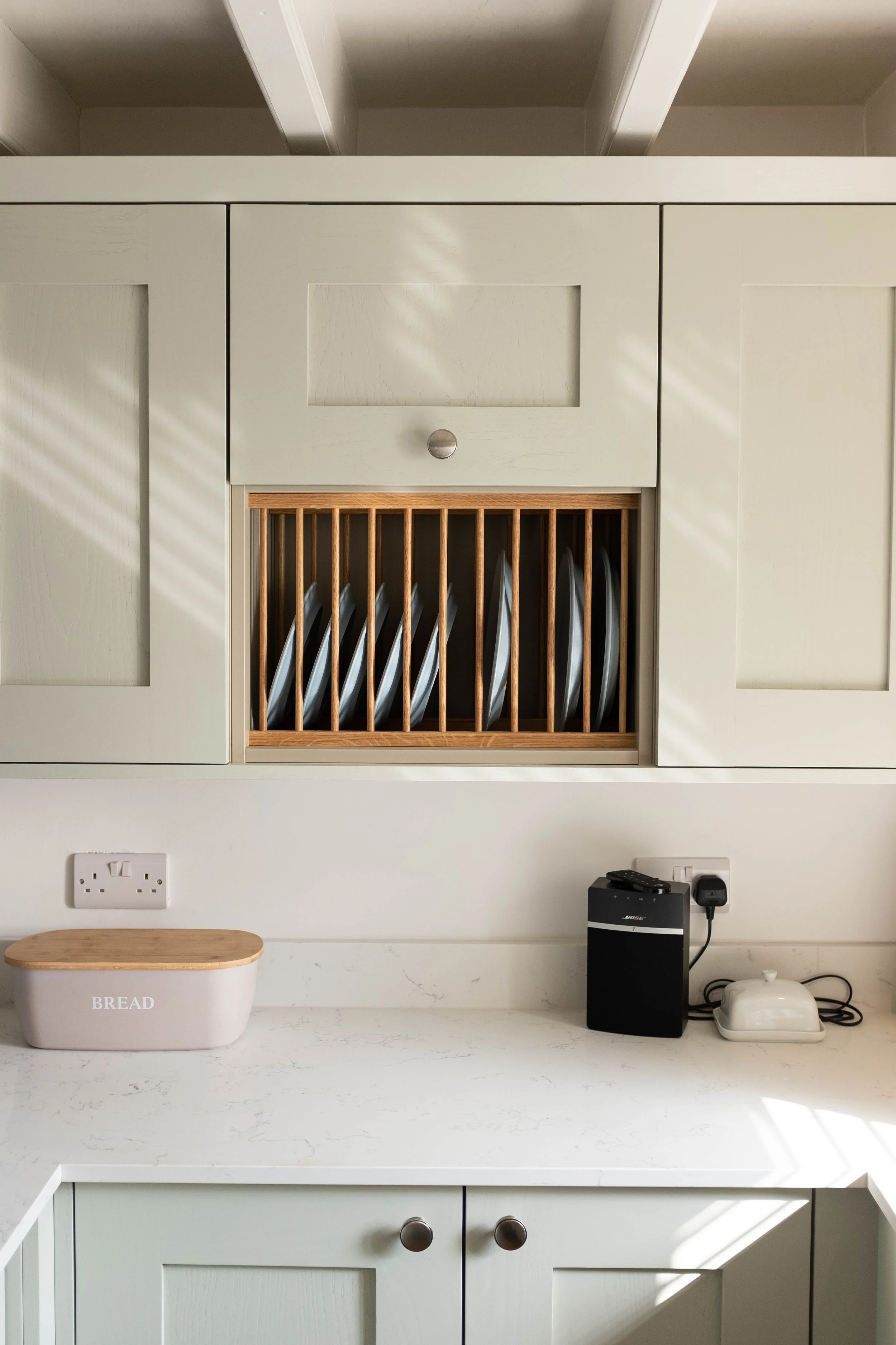 Kitchen wall with cabinets, a bread container, a small black Bose speaker, and an electric kettle on a white countertop.
