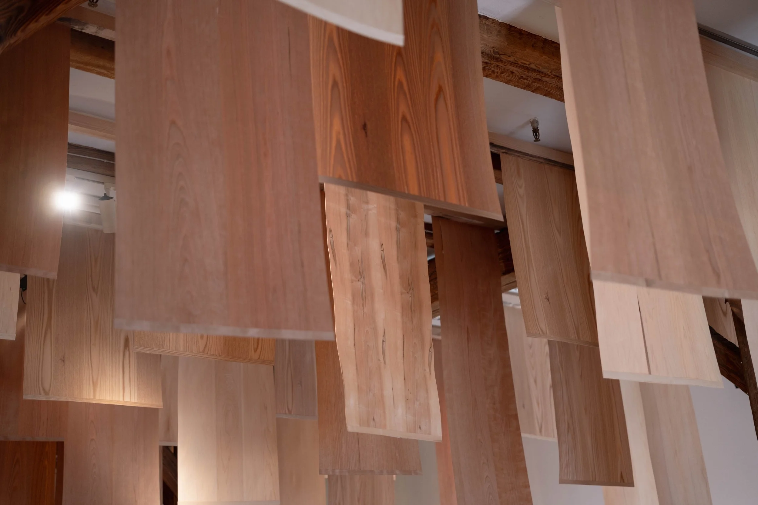 Multiple wooden shelves or panels arranged in an overlapping pattern, made of light-colored wood with visible grain and knots.