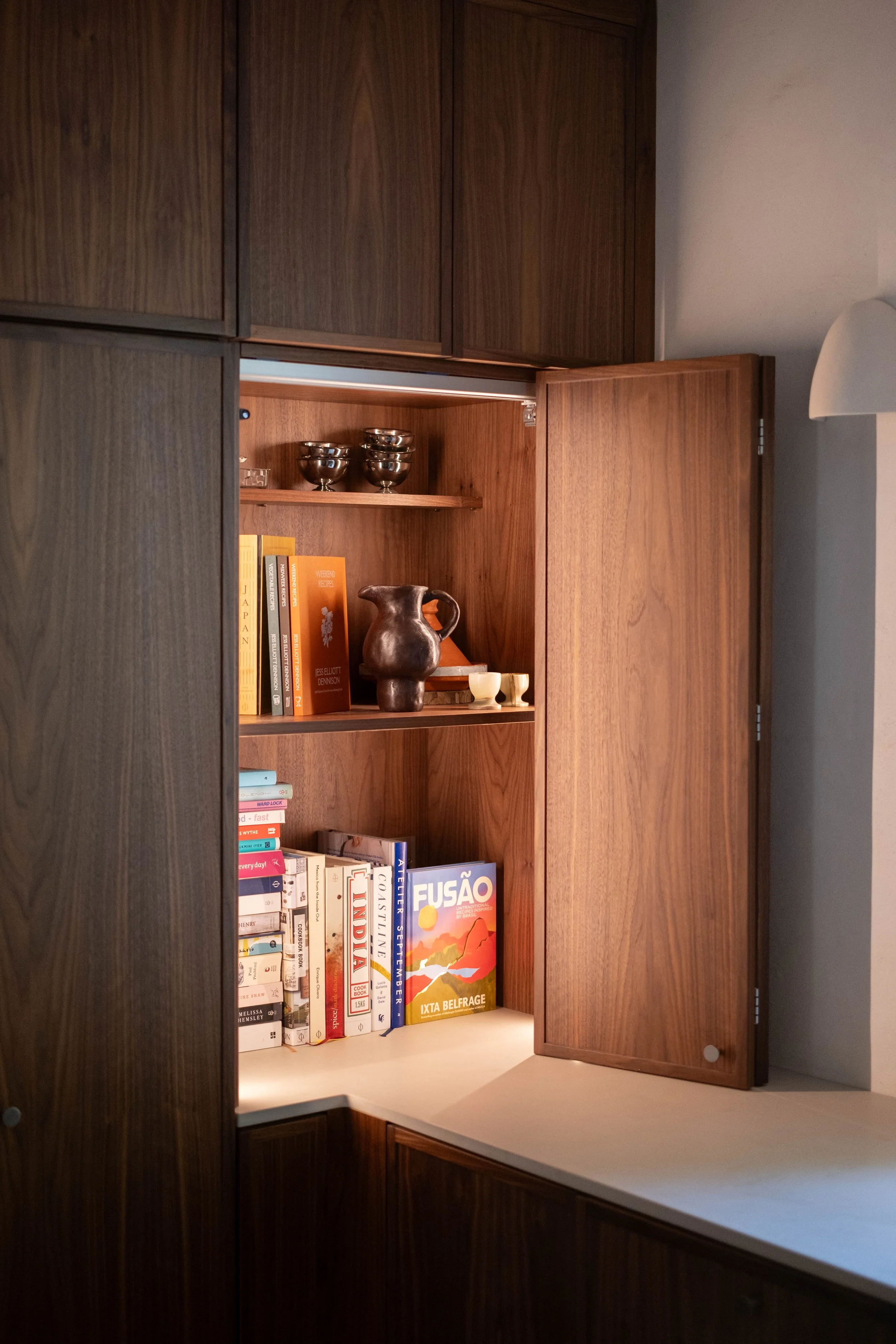 Open wooden cabinet with books, a ceramic pitcher, and metal bowls inside.