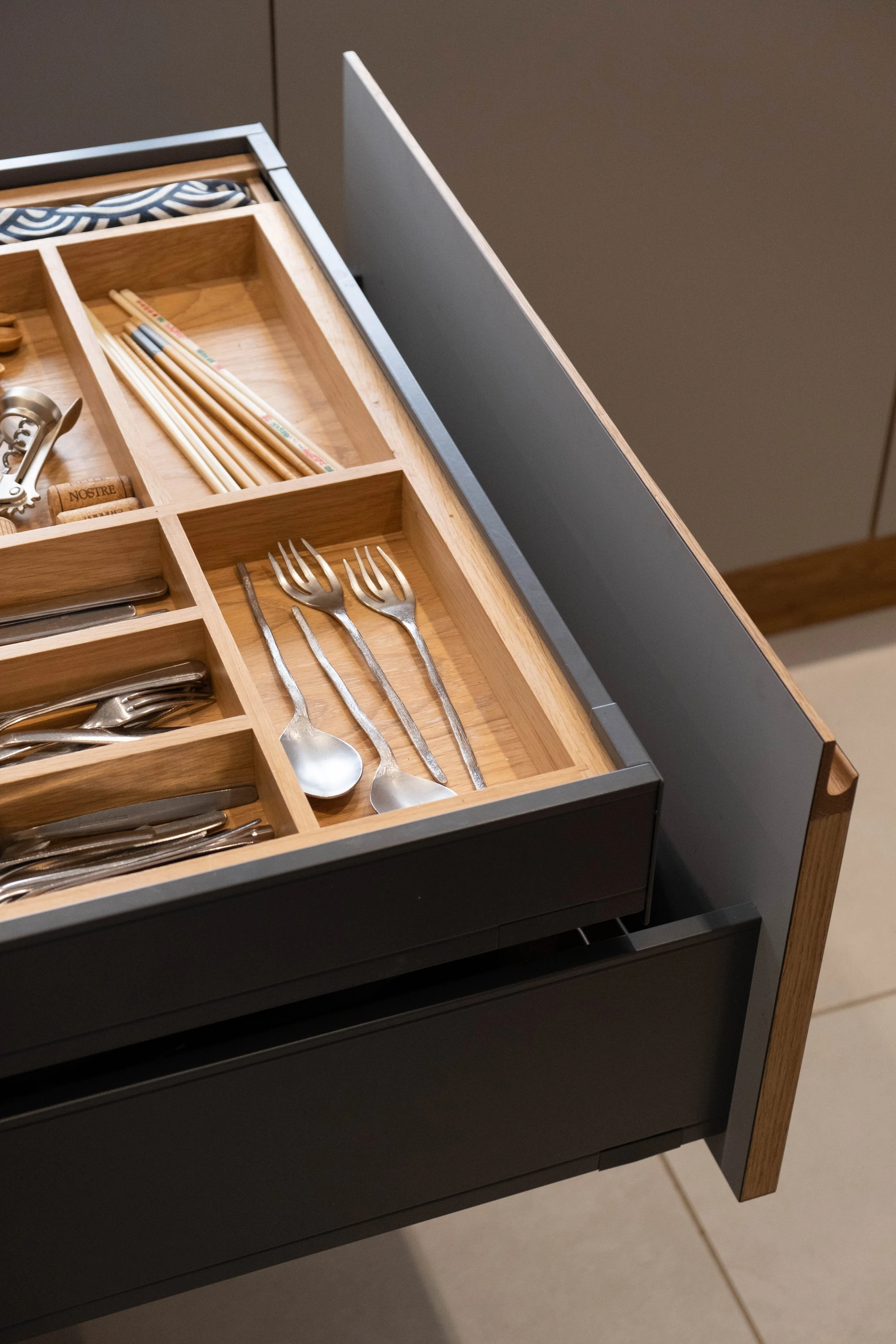 Drawer partially open revealing utensils such as forks and spoons, chopsticks, and various small kitchen tools inside.