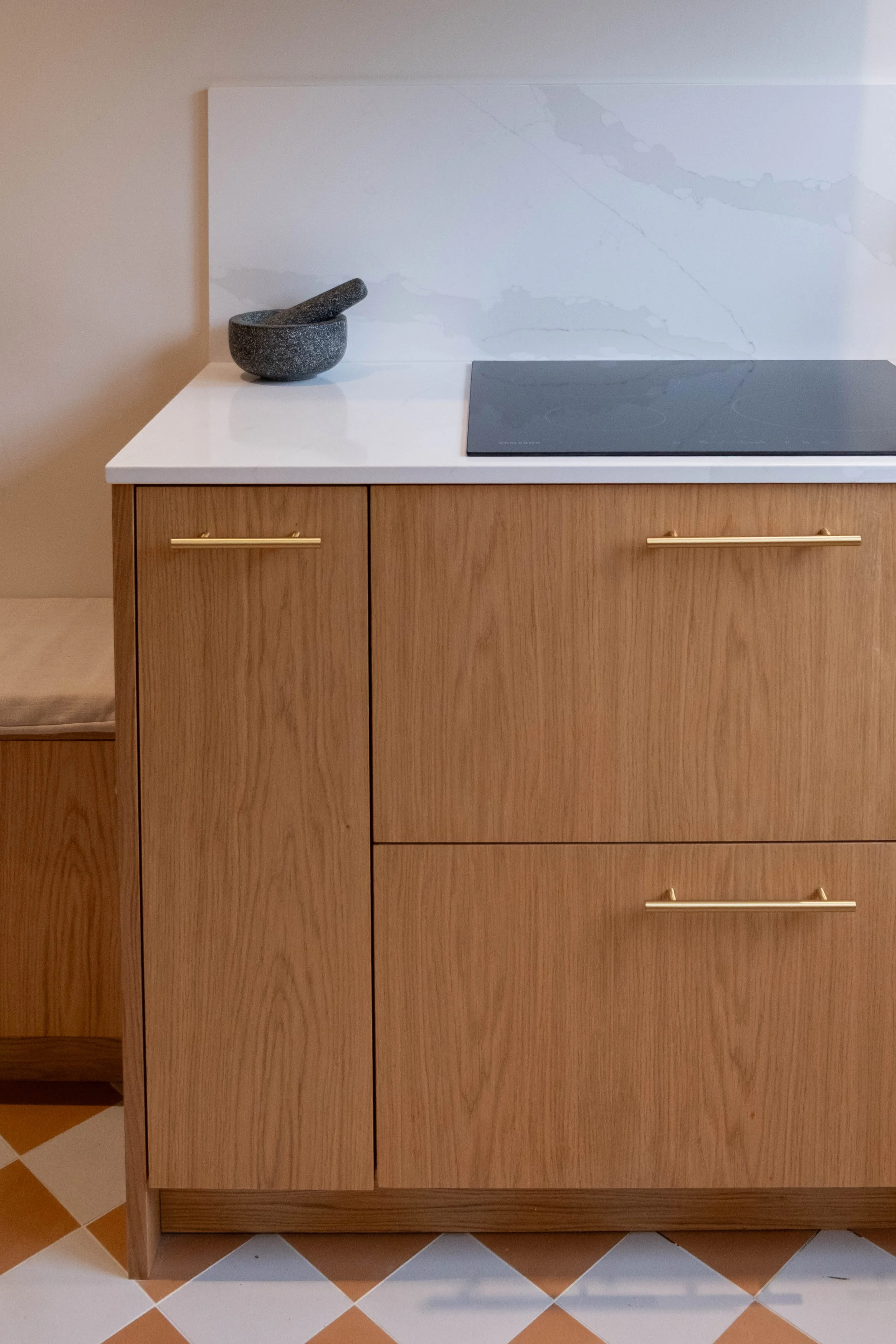 Kitchen counter with a gray mortar and pestle and a black induction cooktop, wooden cabinets with gold handles, and tiled floor.