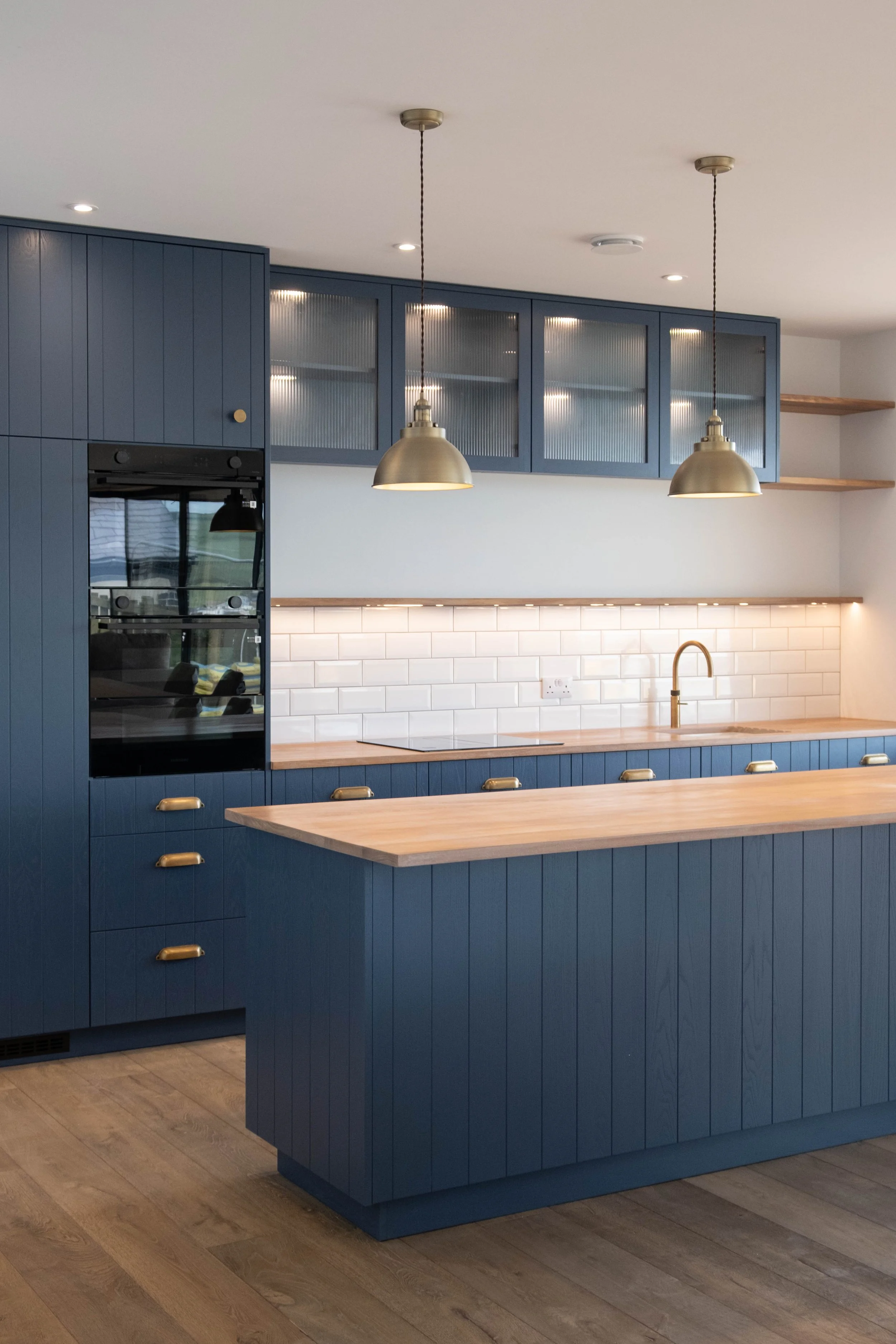 Modern kitchen with navy blue cabinets, a wooden countertop, gold hardware, and pendant lighting.