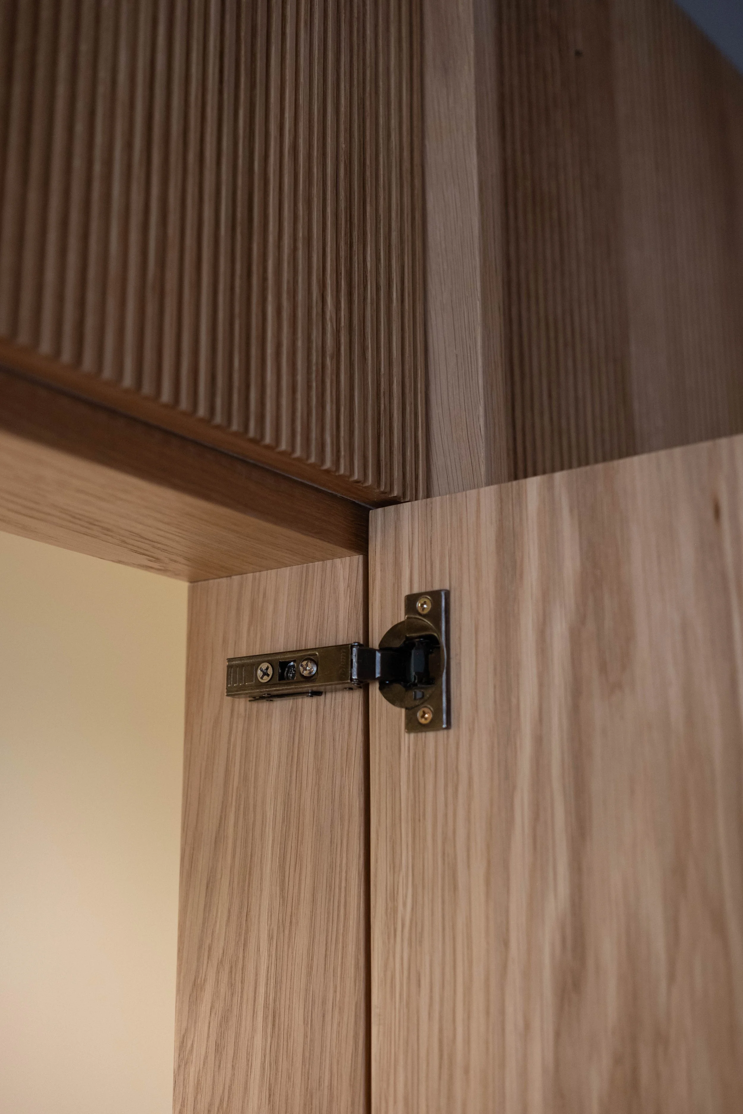 Close-up of the corner of a wooden cabinet door with a metal hinge.