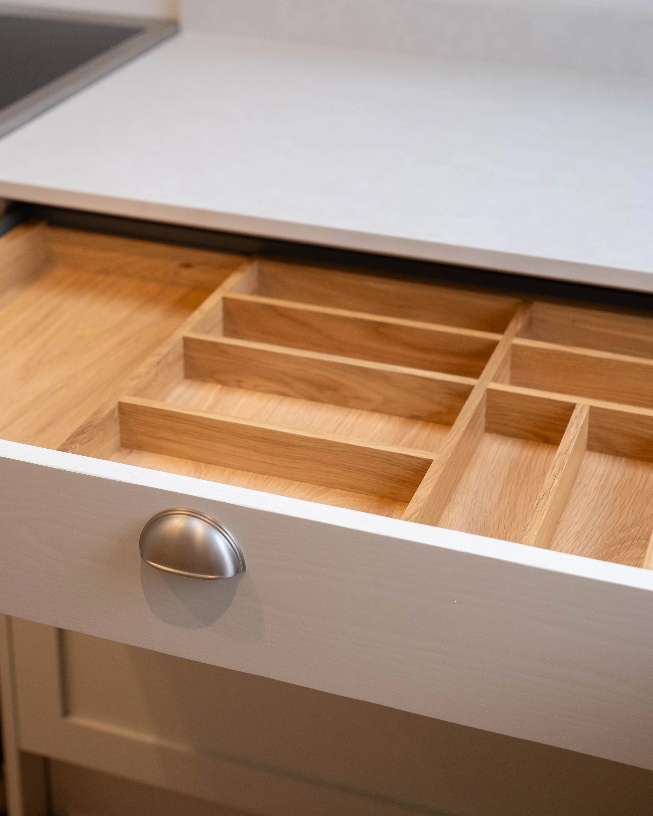 Close-up of a white kitchen drawer with a metallic knob, partially open to reveal empty wooden compartments inside.