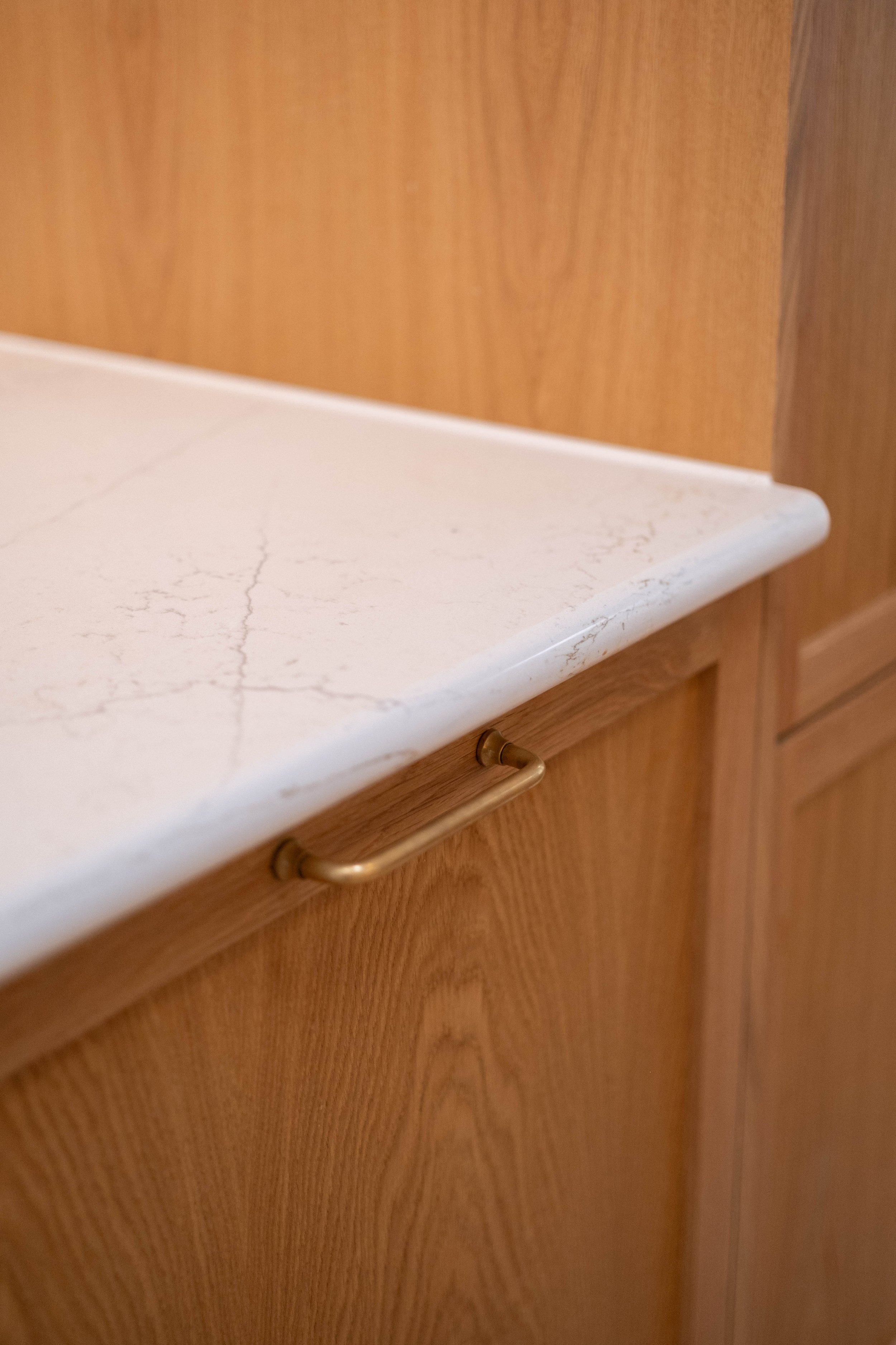 Close-up view of a kitchen countertop made of white marble with subtle gray veining and a wooden cabinet with a curved brass handle.