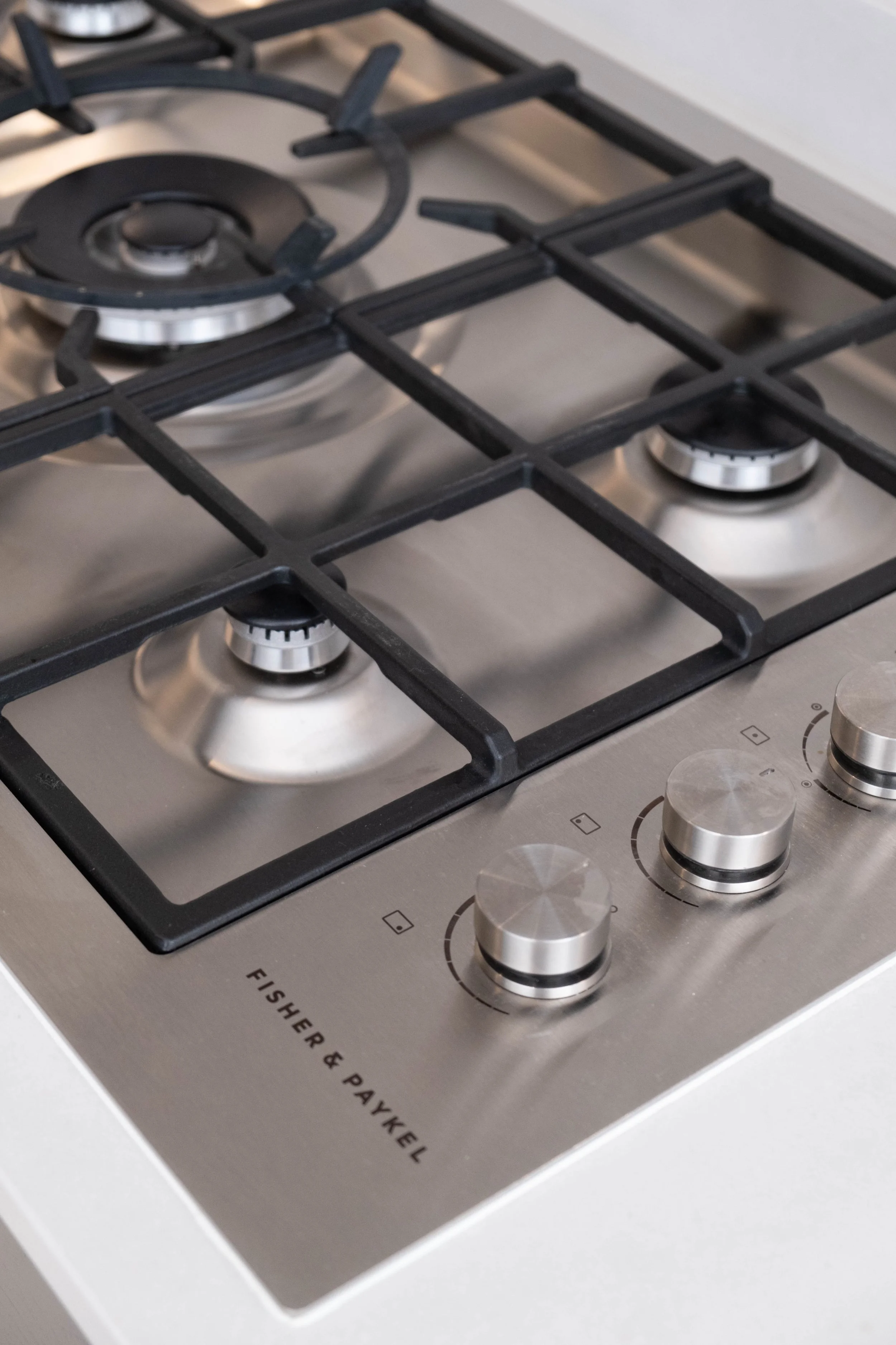 Close-up of a stainless steel gas stove with three burners and control knobs, with the logo 'Fisher & Paykel' visible on the surface.
