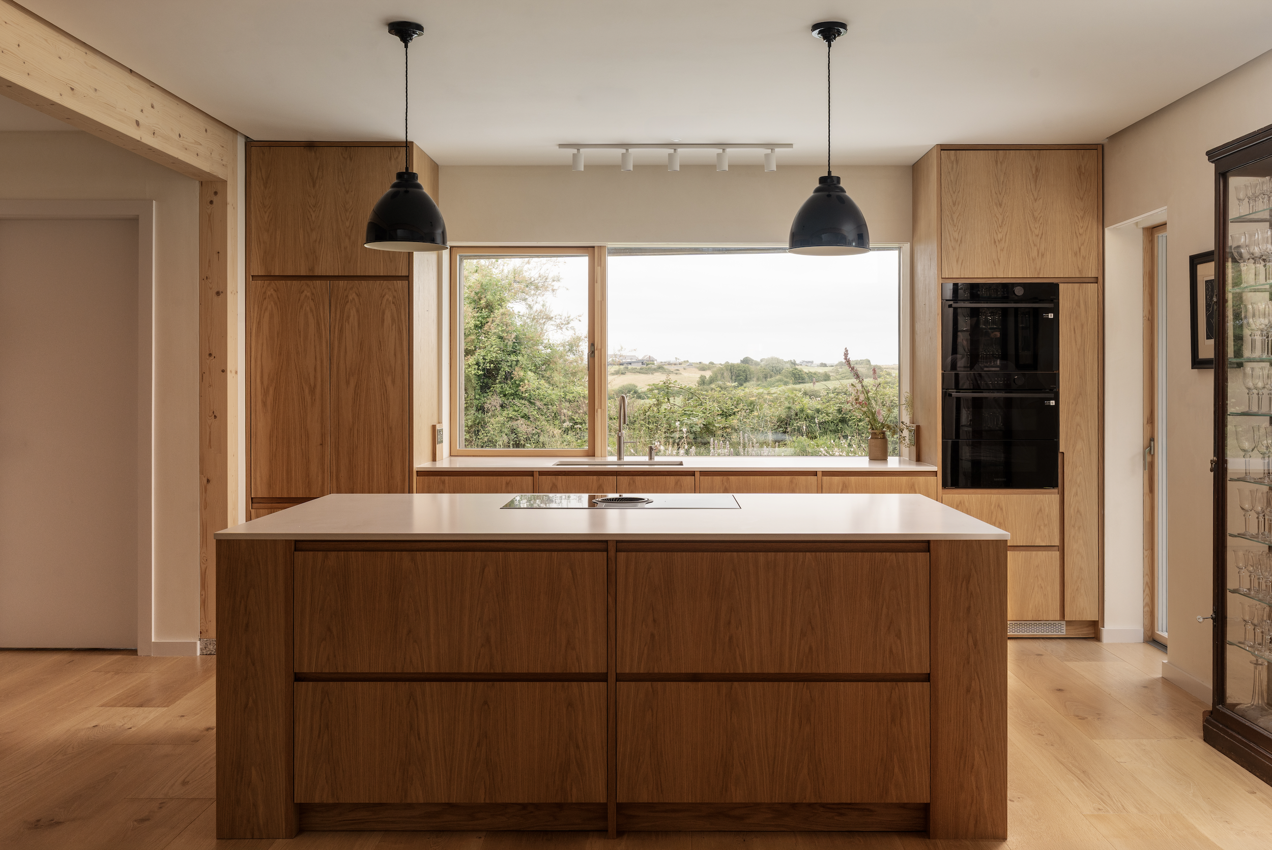 Modern kitchen with wooden cabinets, a large window overlooking a landscape, and a kitchen island with an electric stove.