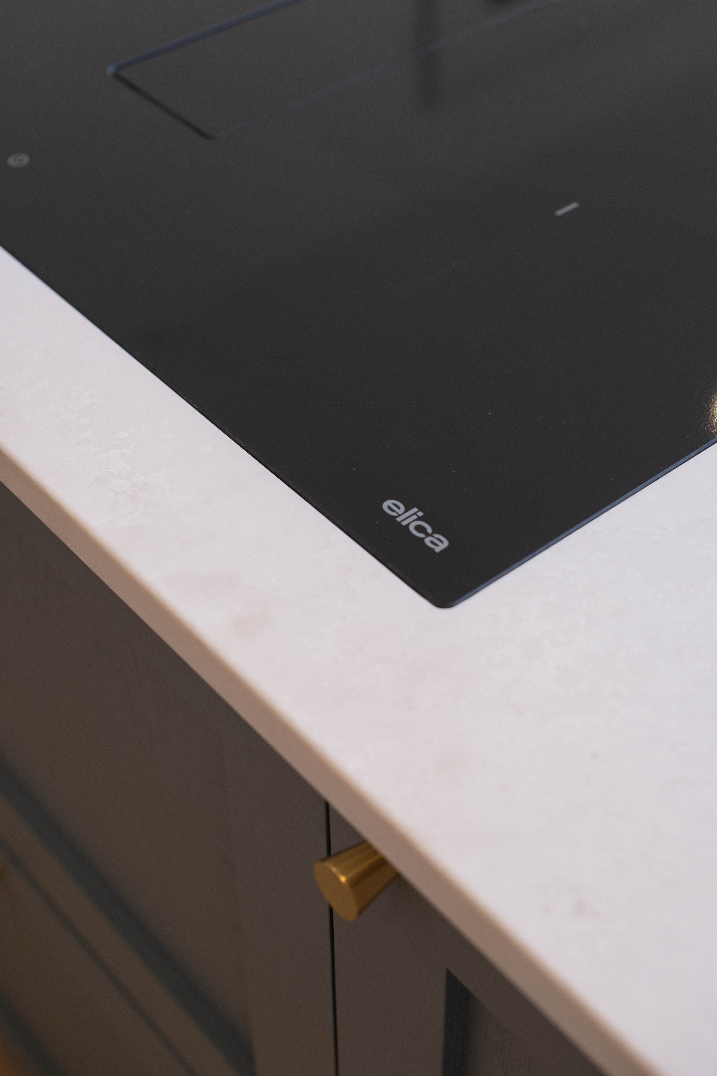 Close-up of a black tabletop with a white edge, part of a gray cabinet or drawer unit beneath it, with a gold-colored handle visible on one of the drawers.