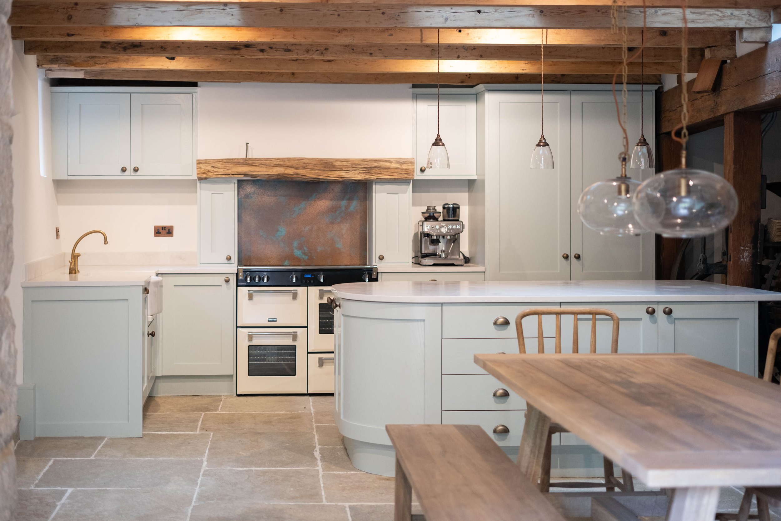 A kitchen with white cabinetry, a gold faucet, a stove, a coffee machine, and hanging pendant lights, with a wooden ceiling and a tiled floor.