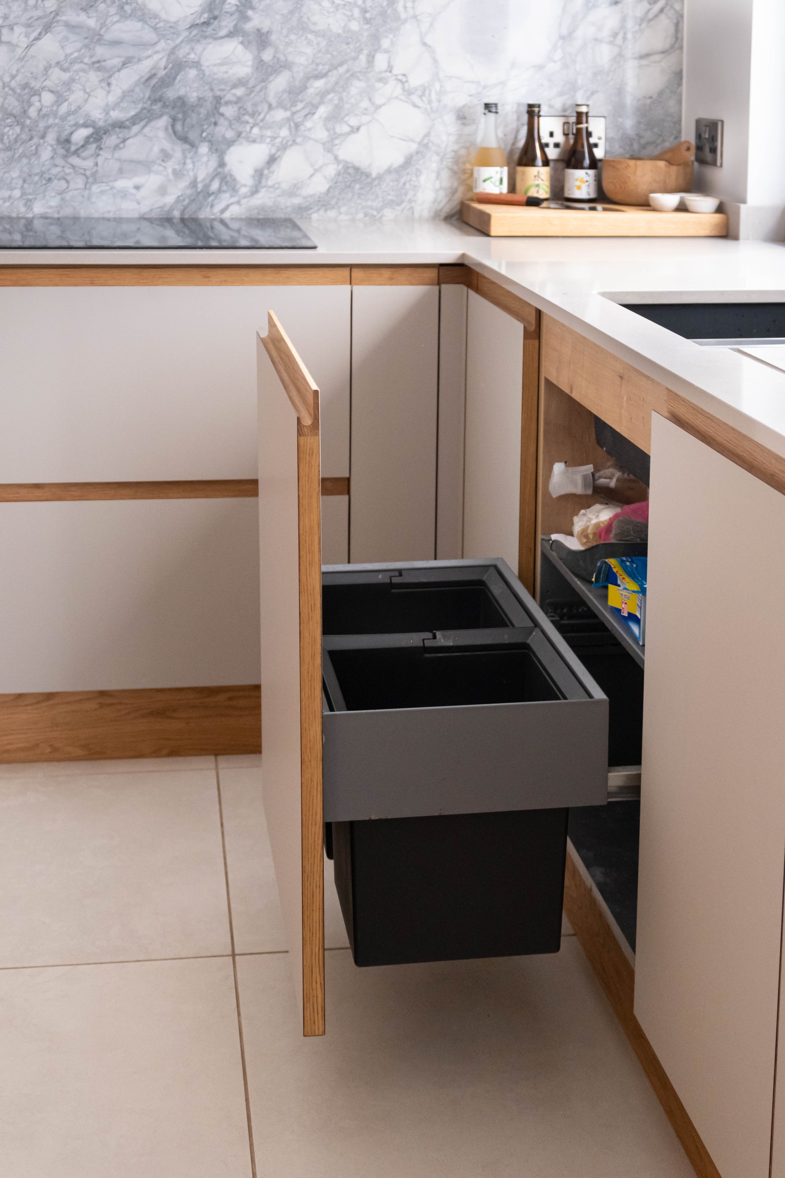 Kitchen with white countertops, wooden accents, marble backsplash, and open cabinet drawers containing utensils and supplies.