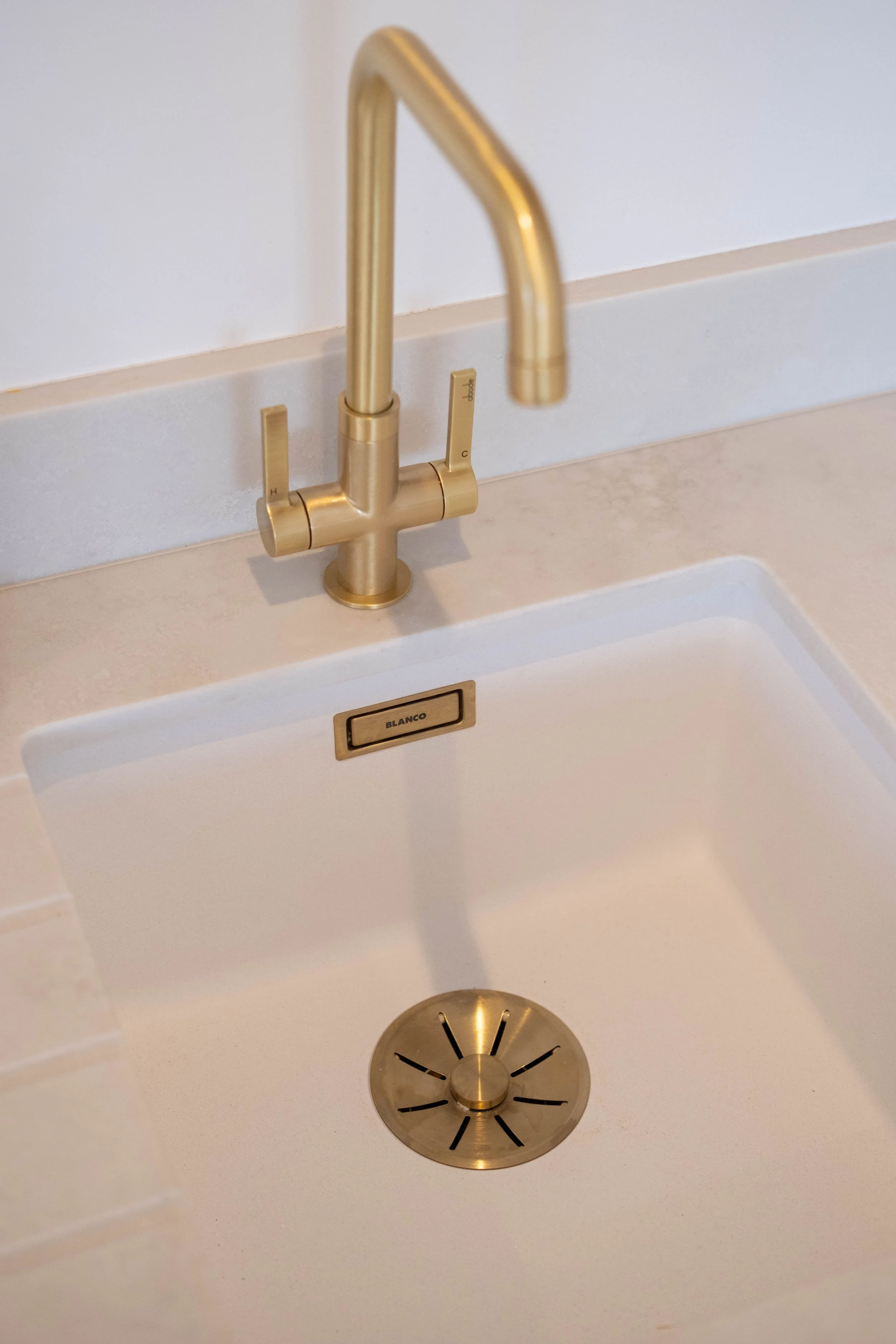 A gold-colored kitchen faucet with two handles above a white sink, with a circular drain cover below.