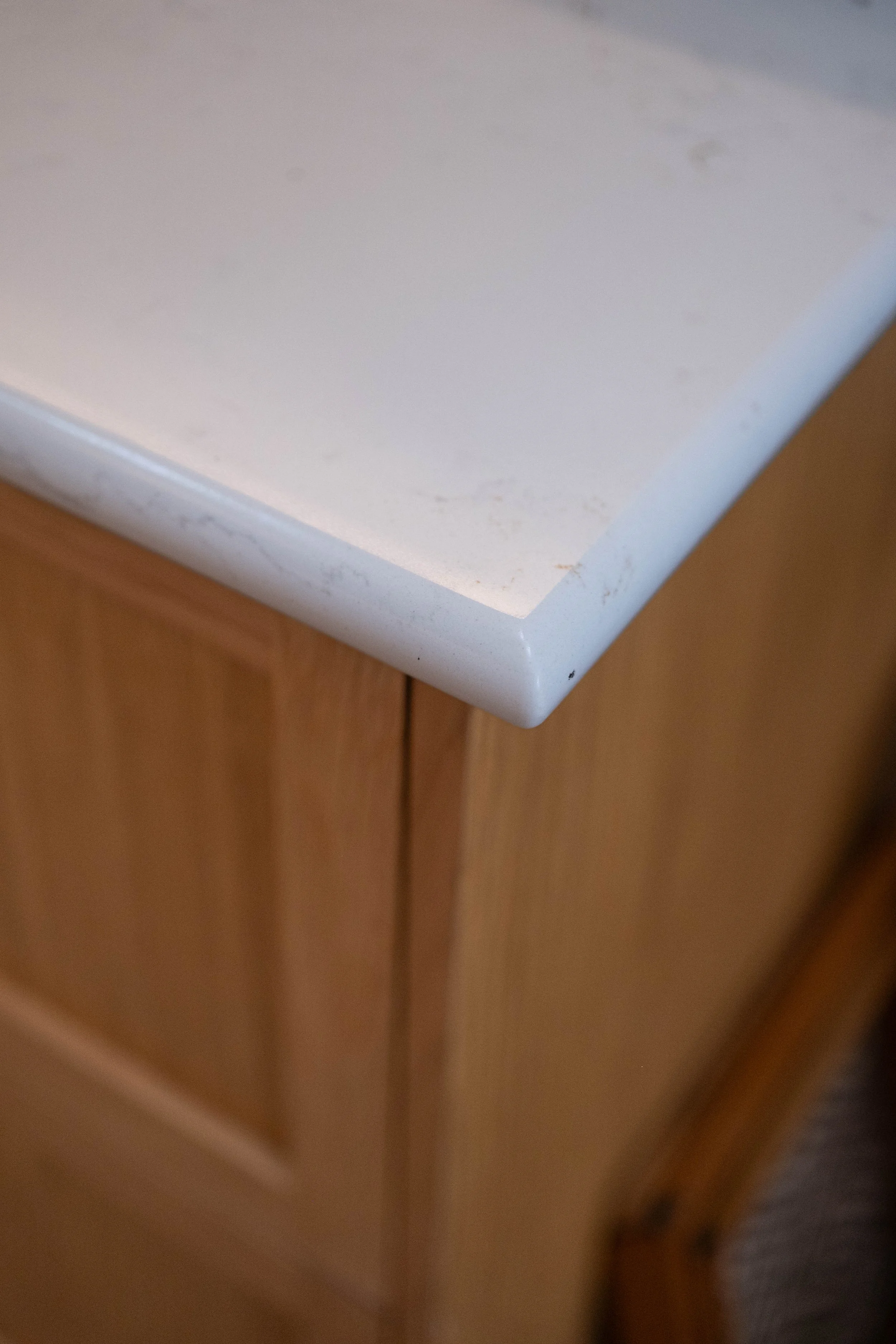 Close-up of the corner of a white kitchen countertop with a wooden cabinet underneath.