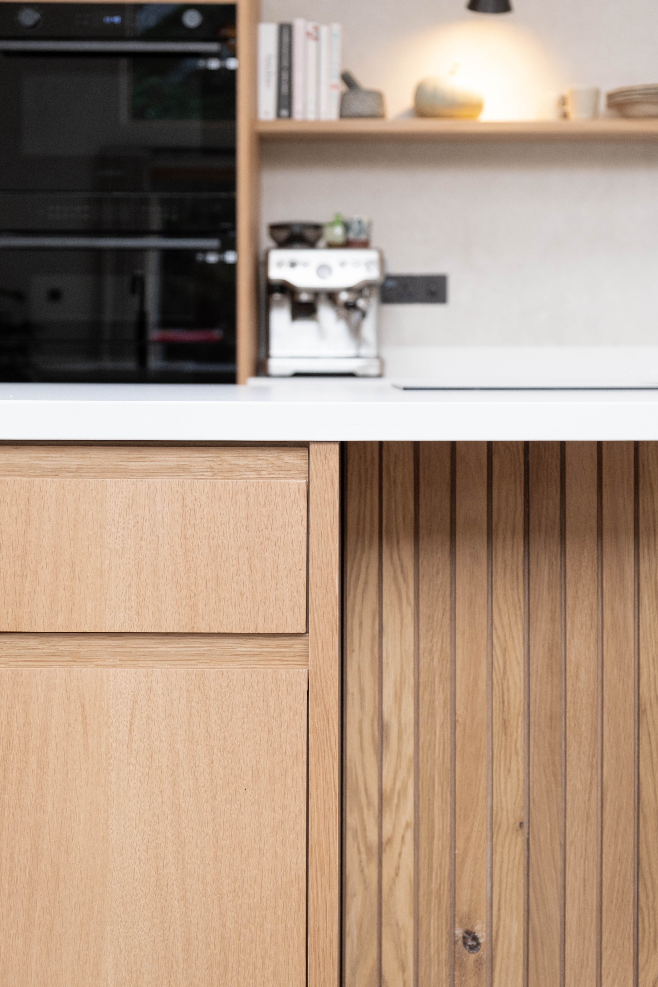 A kitchen counter with wooden cabinets, a coffee machine, a shelf with books, and a stove on the left side.