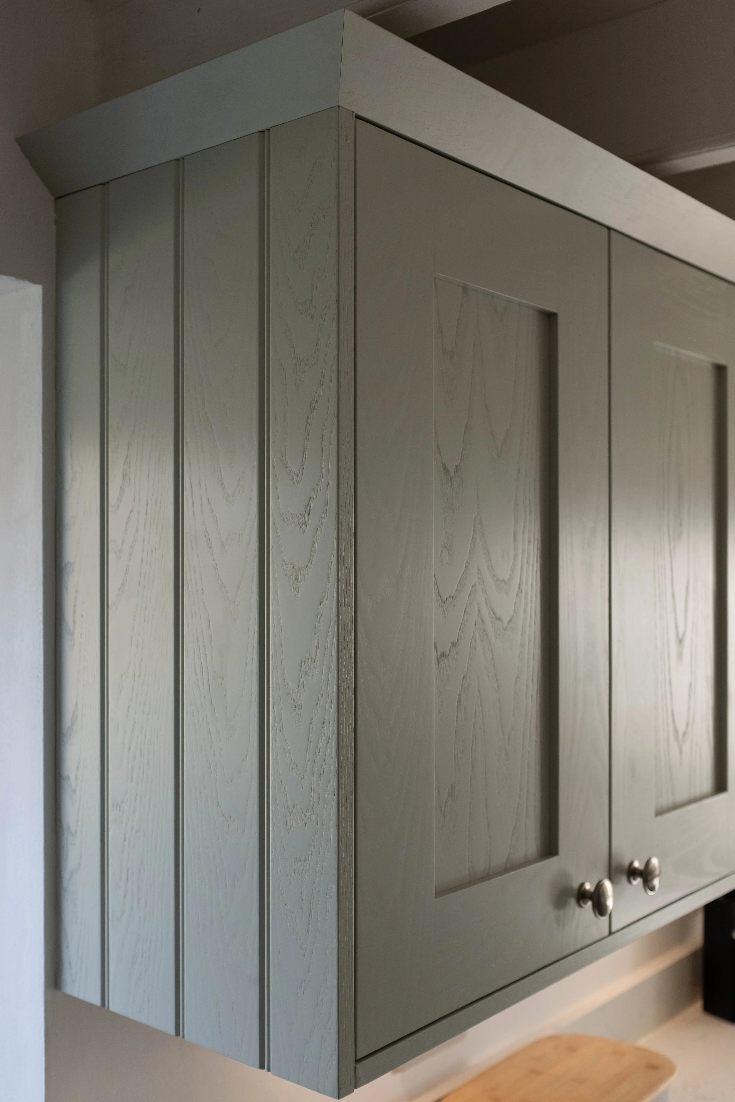 Light gray wooden cabinet with vertical panels and silver knobs, mounted on a wall in a room with a wooden ceiling.