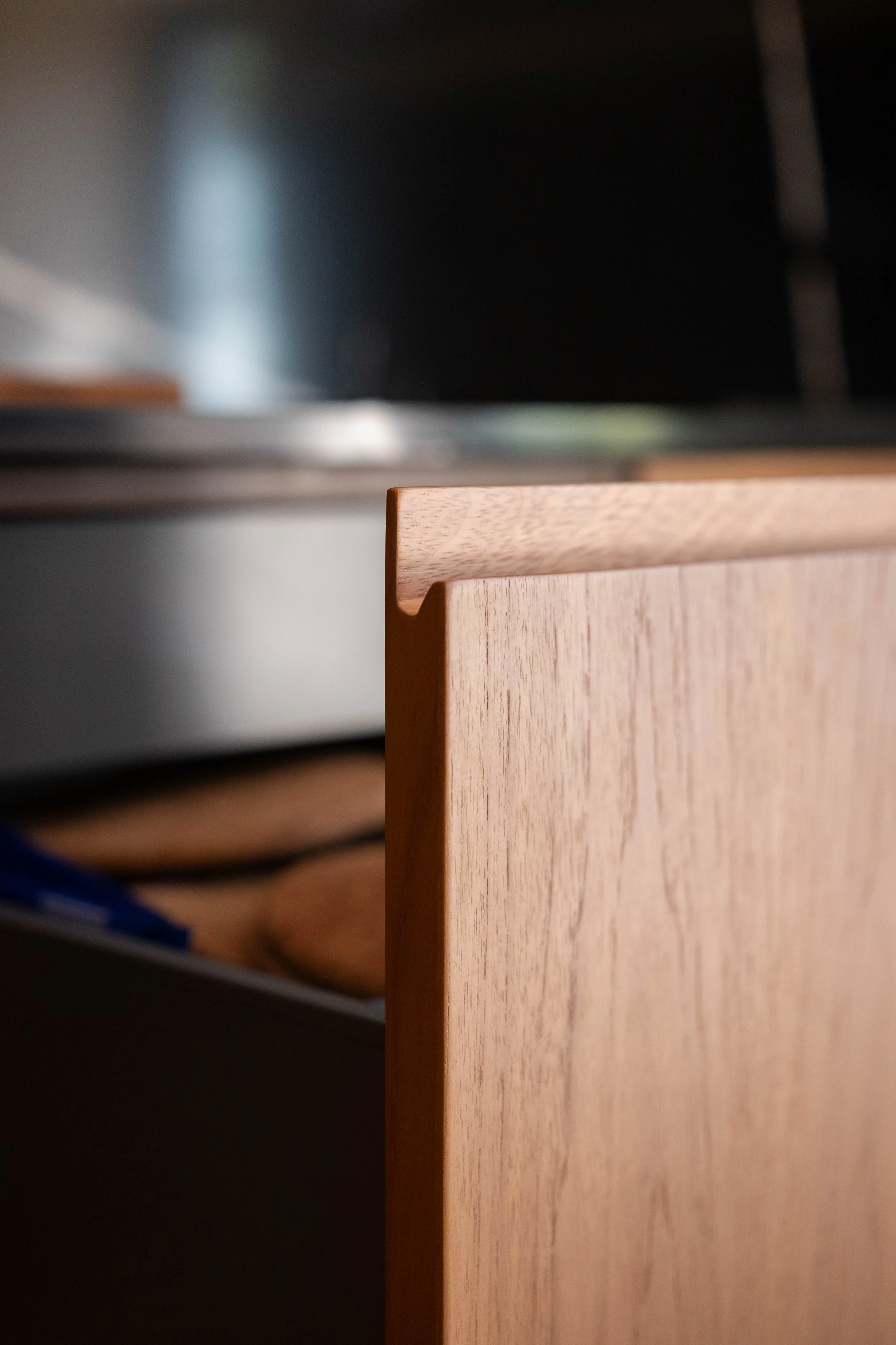 Close-up of the corner of a wooden desk or cabinet with a smooth, natural finish, part of a grey wall, and a dark background